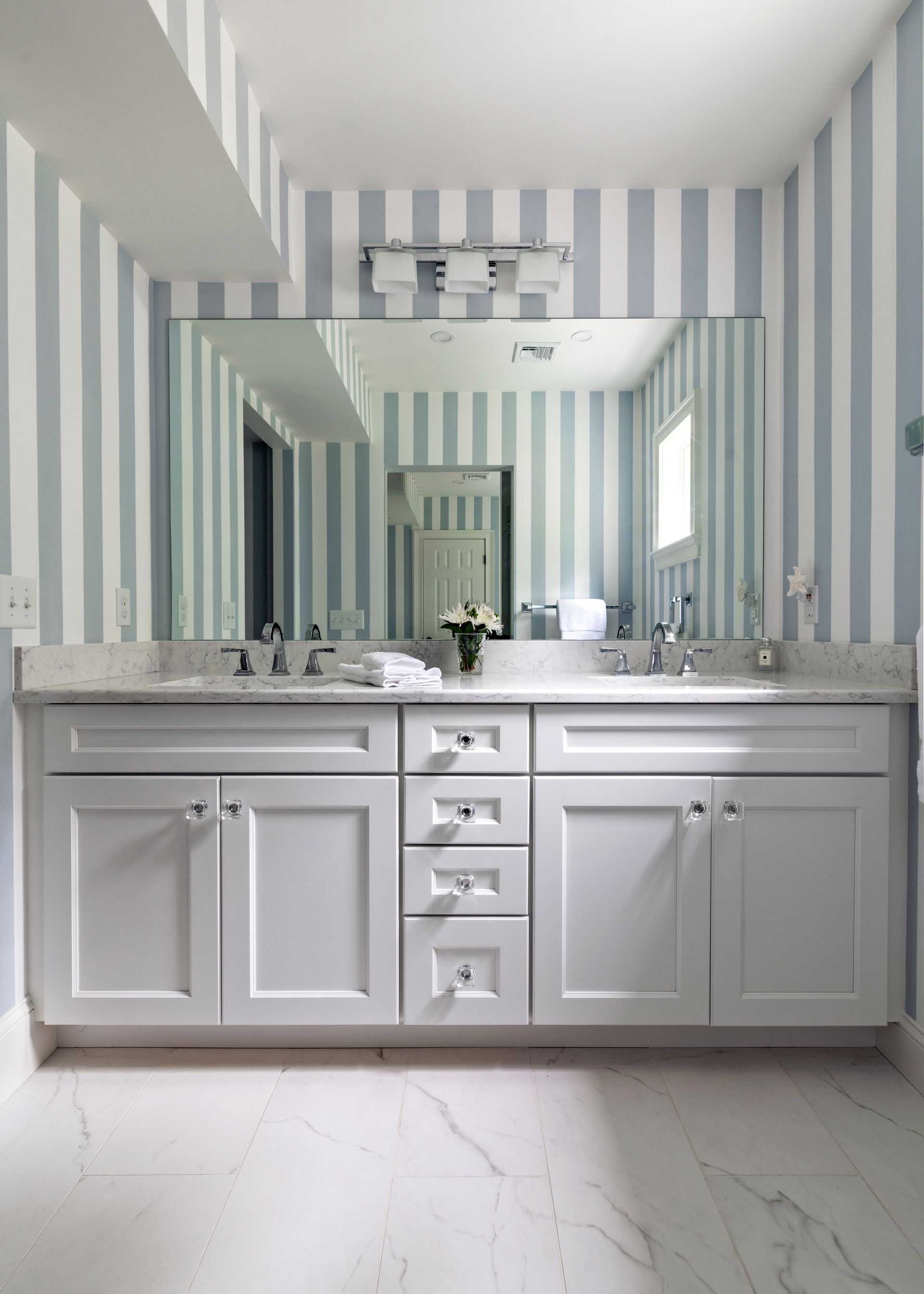 White bathroom vanity with dual sinks, large mirror, and blue-and-white striped wallpaper