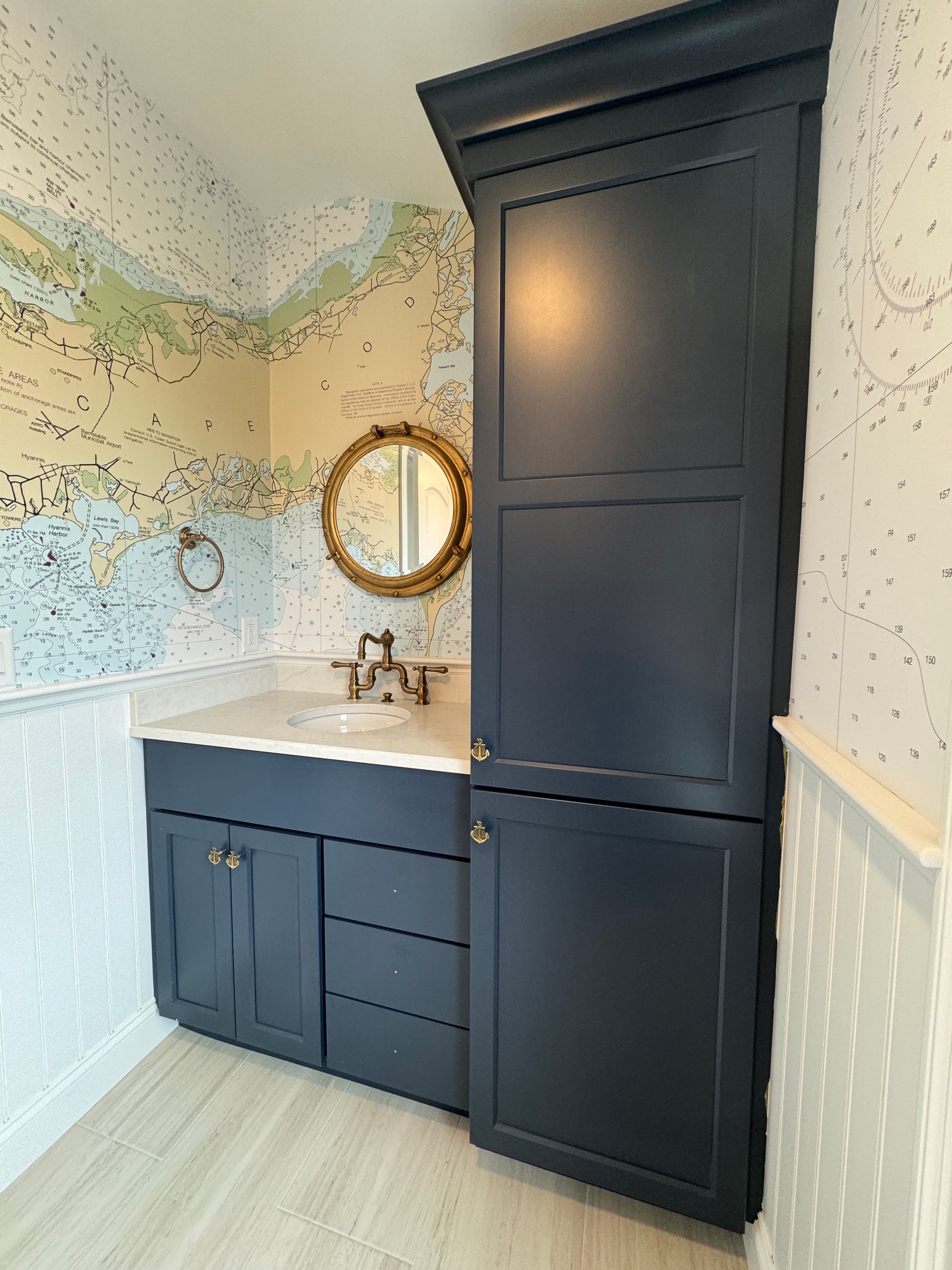 Navy blue bathroom vanity with white countertop, round gold mirror, and patterned wallpaper.