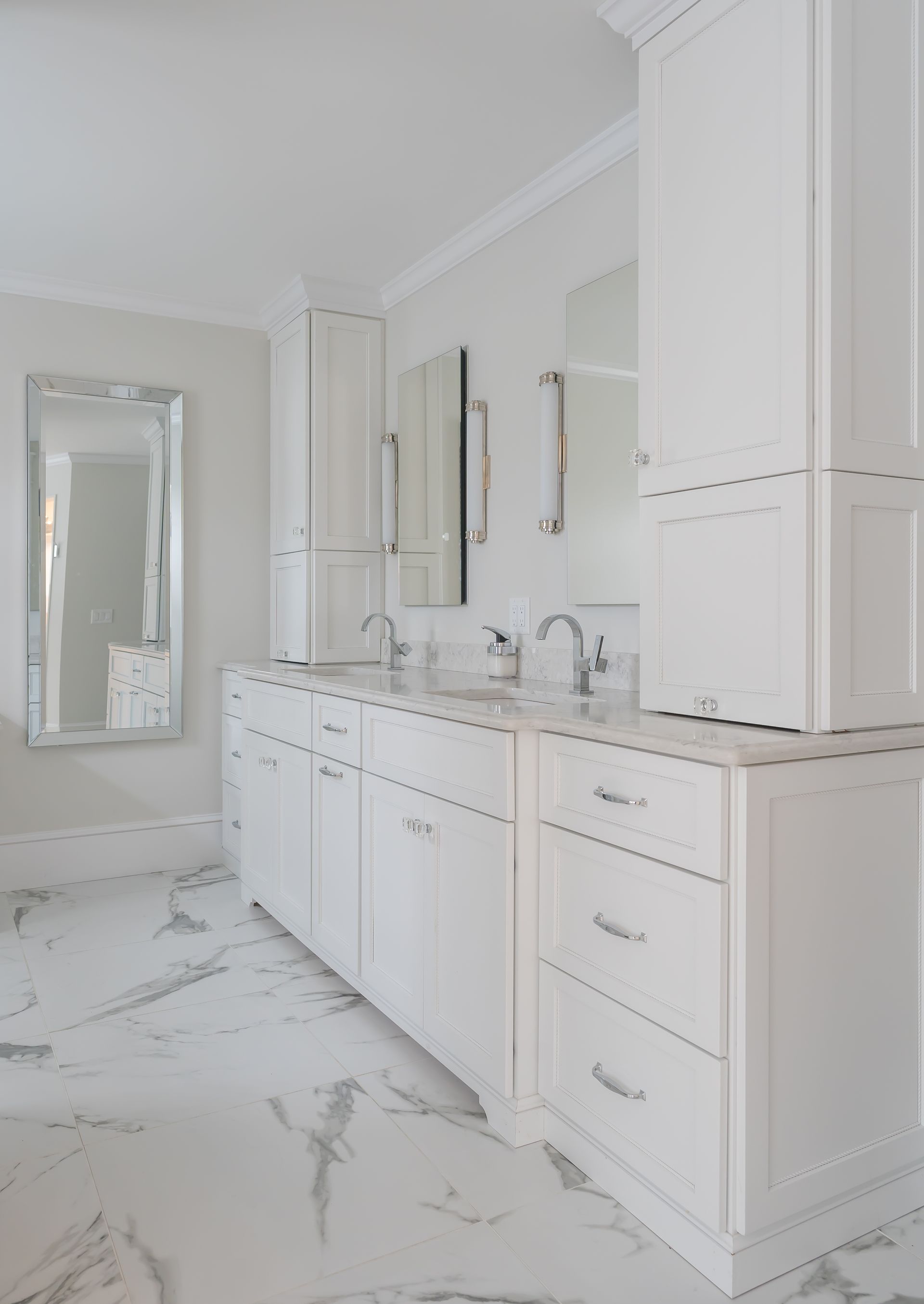 Bright white bathroom with marble flooring, double vanity, mirrors, and a shower enclosure