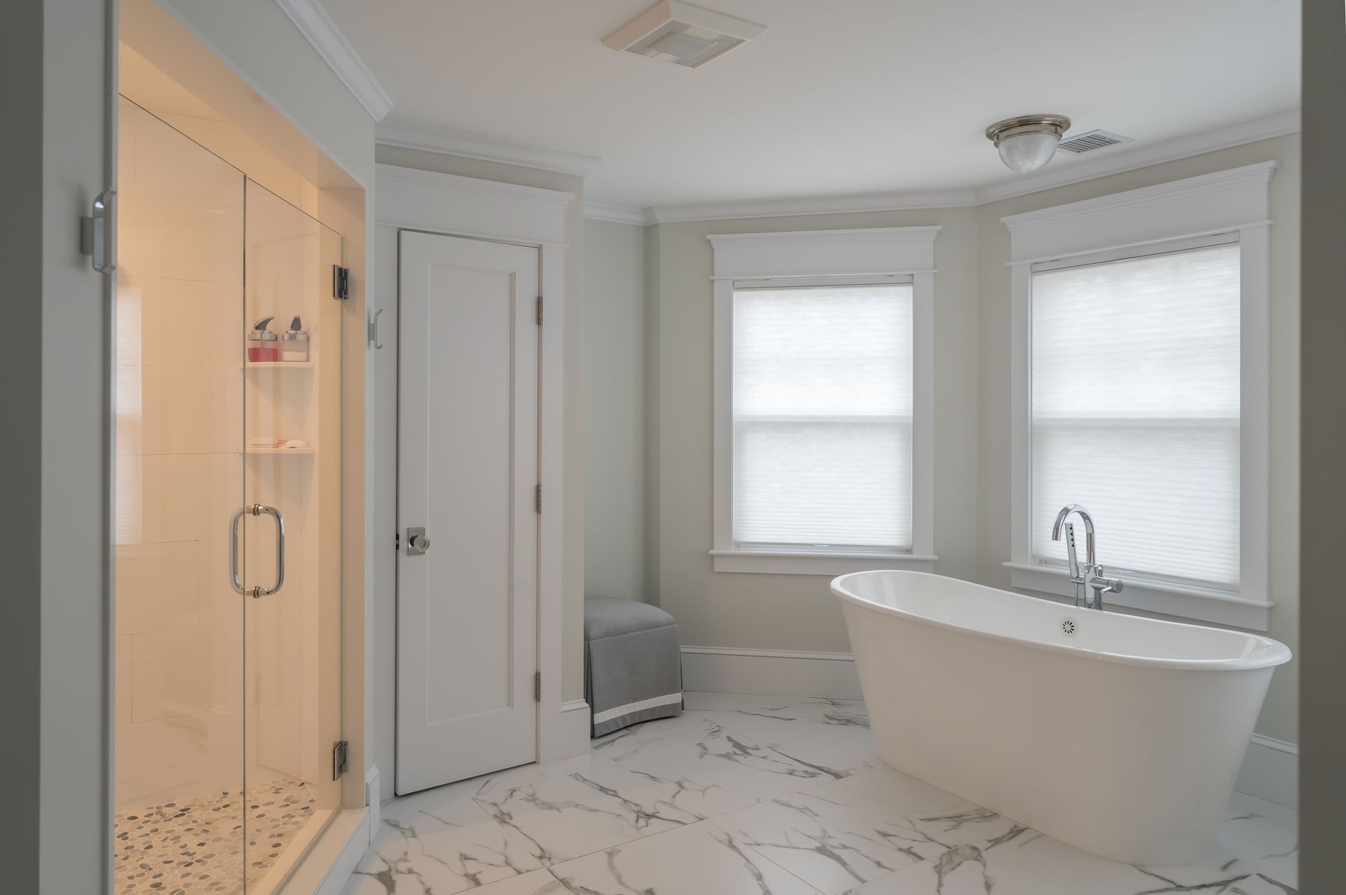 Modern bathroom with freestanding tub, glass shower, double windows, and marble-pattern tile floor