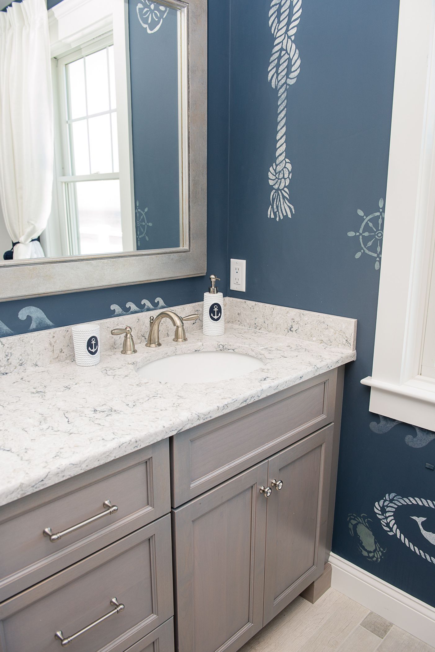 Bathroom vanity with gray cabinets, white marble countertop, and navy patterned wallpaper beside a window.