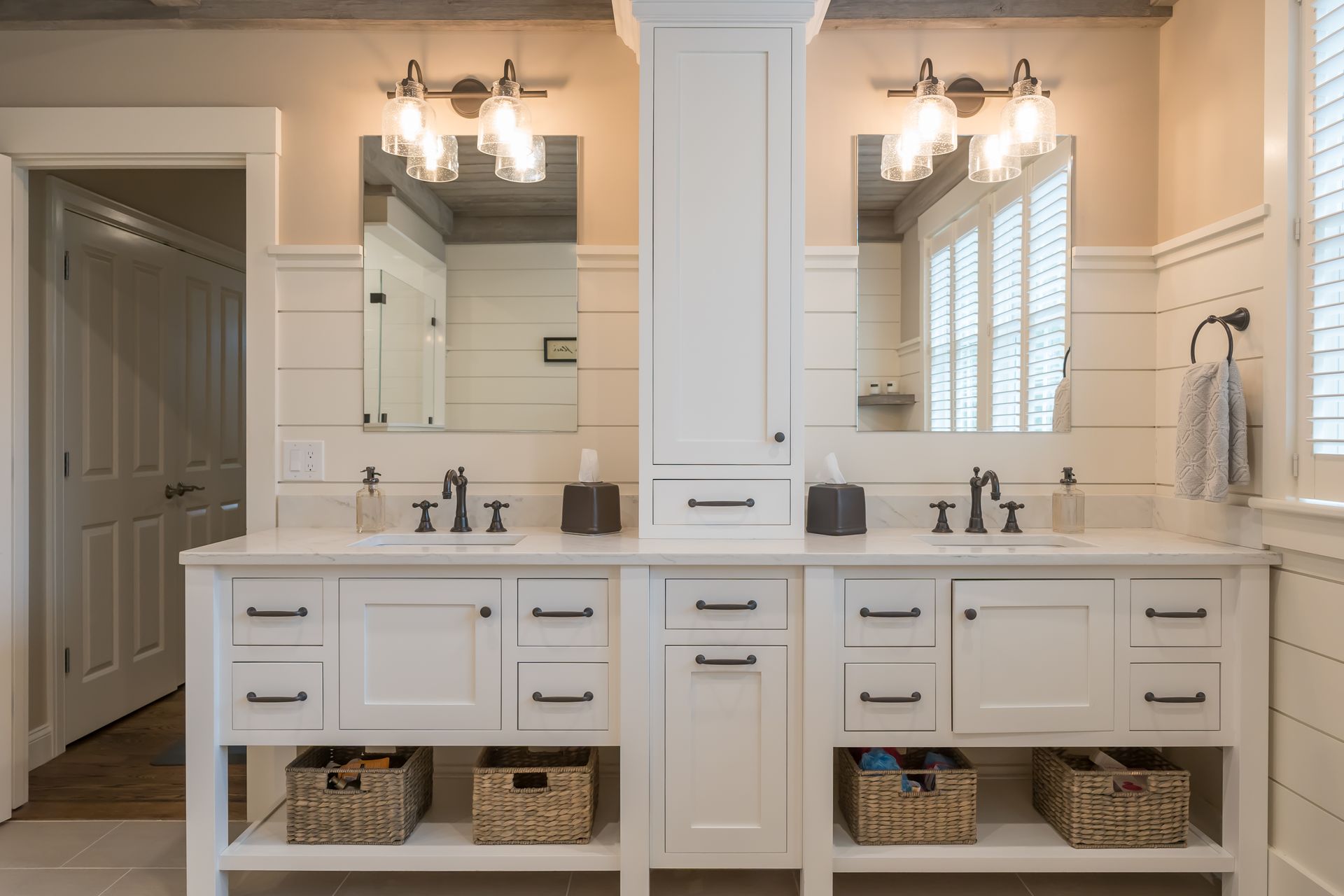 Bright white double bathroom vanity with mirrors, sconces, sinks, and woven baskets underneath