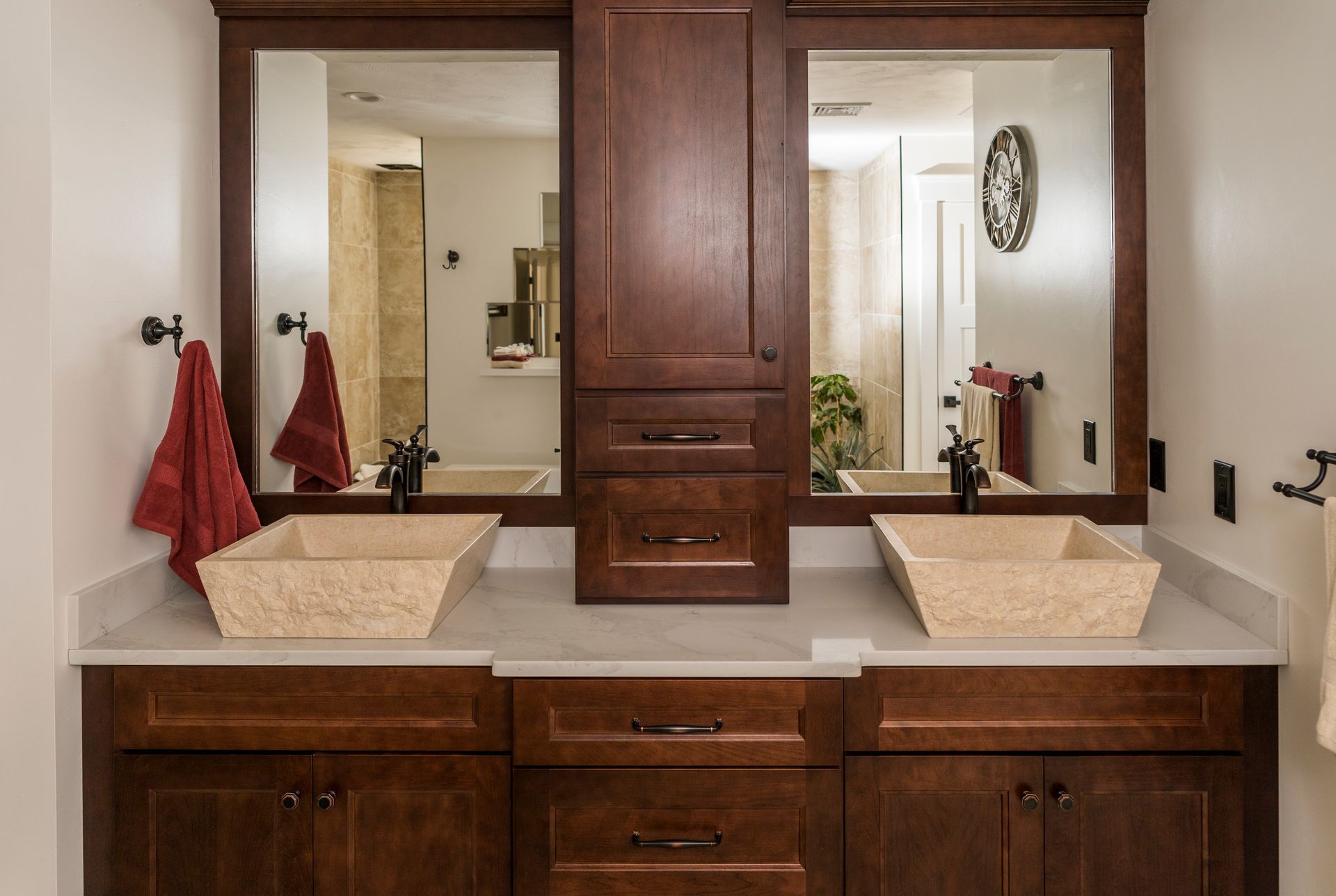 Double vanity bathroom with wood cabinets, stone sinks, and large mirrors under warm lighting