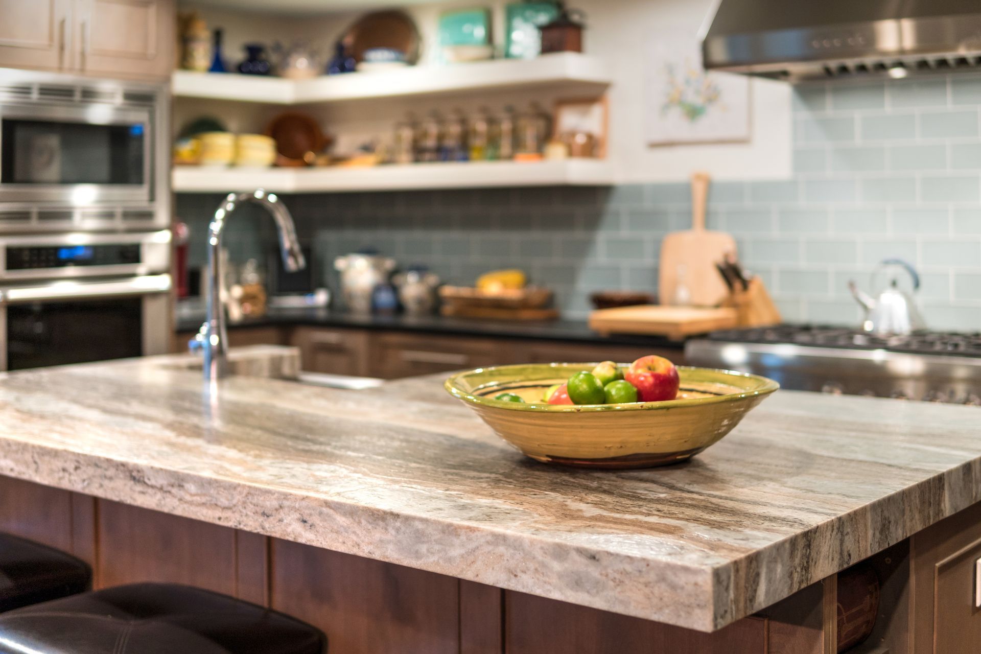 Modern kitchen with a stone island and a bowl of fruit in the foreground