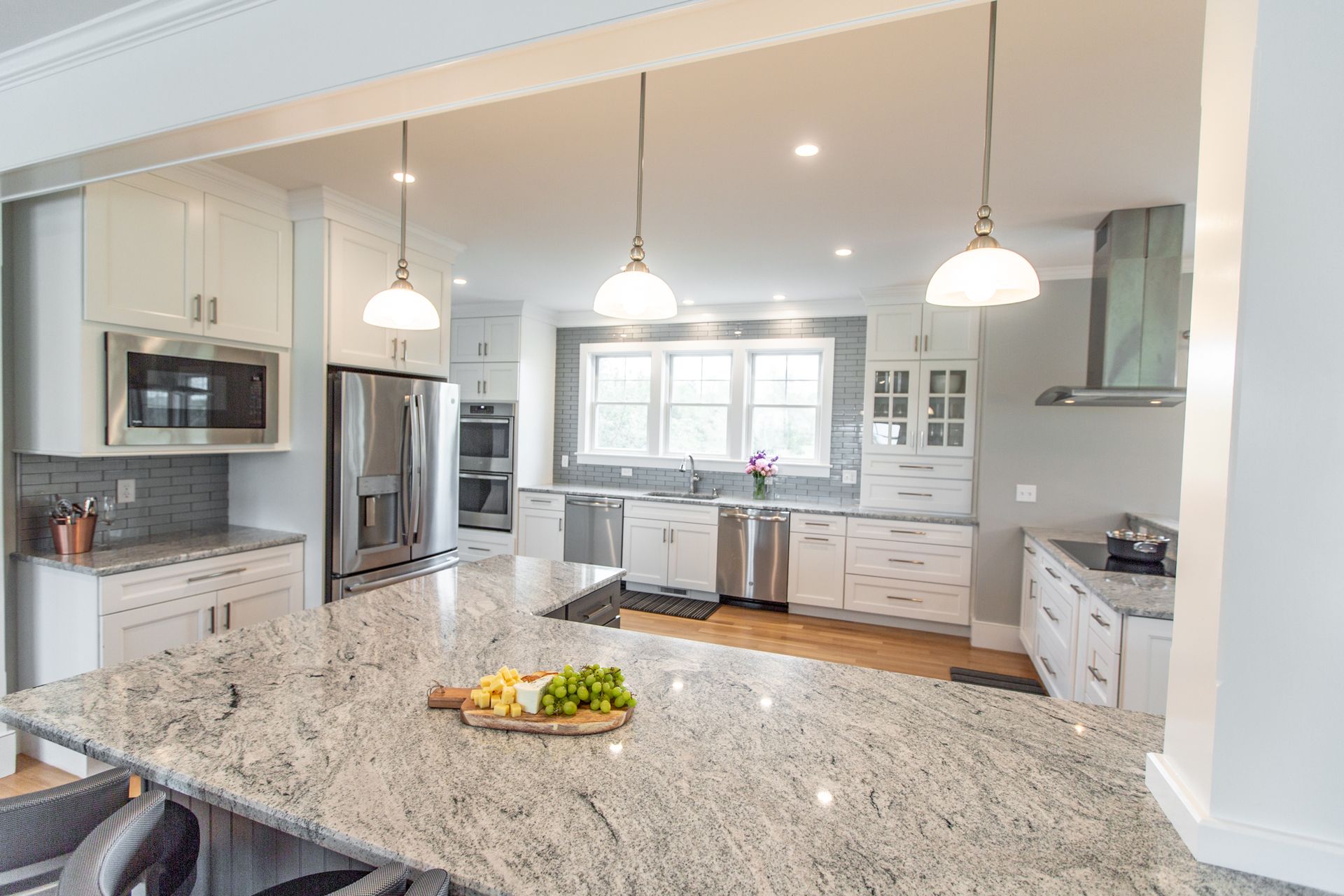 Bright modern kitchen with granite island, stainless appliances, pendant lights, and a bowl of fruit