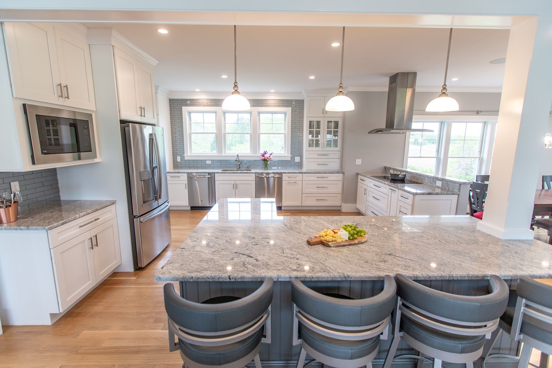 Bright modern kitchen with white cabinets, stainless appliances, and a large granite island with bar stools