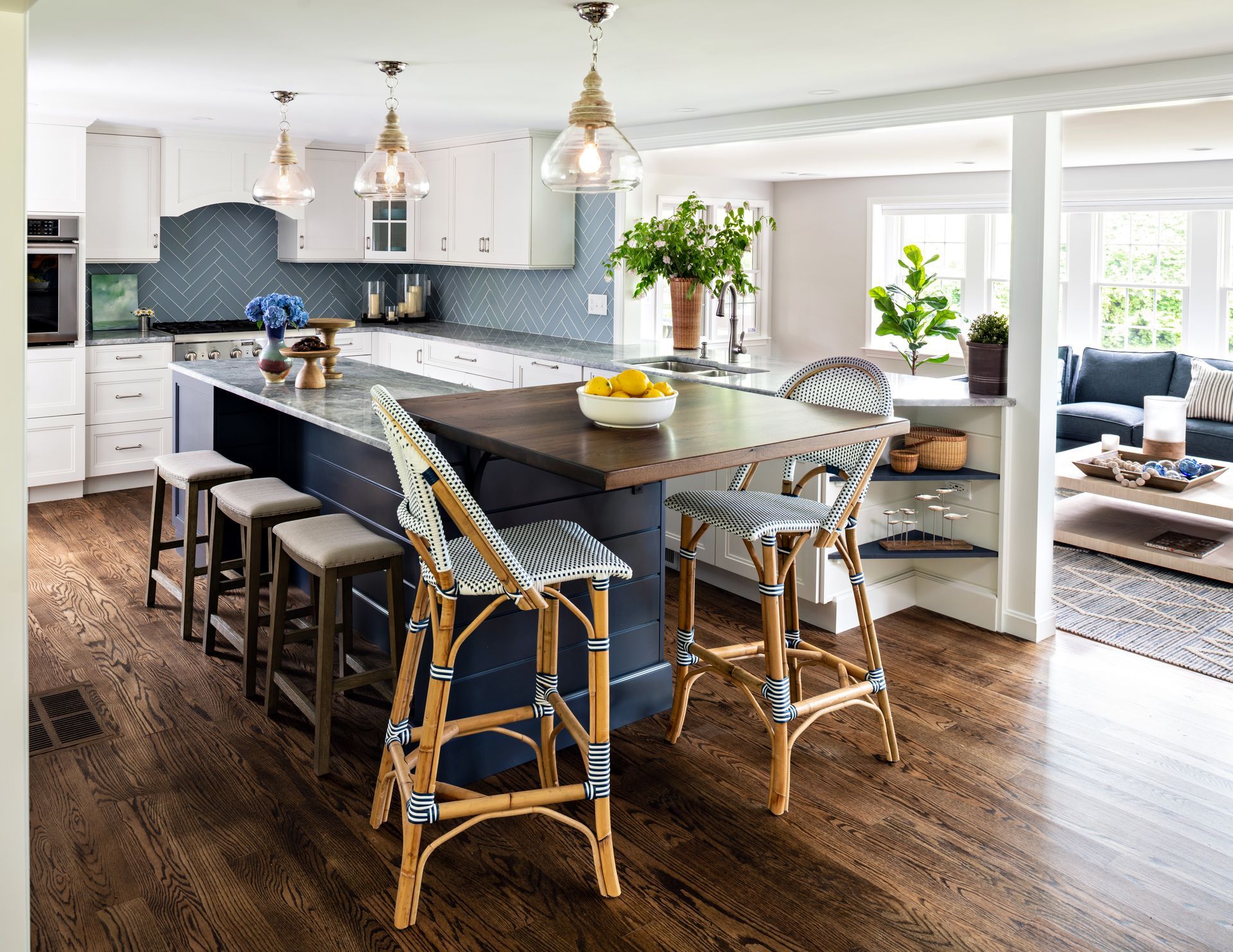 Bright kitchen with blue island, pendant lights, wooden stools, and large windows overlooking a living room