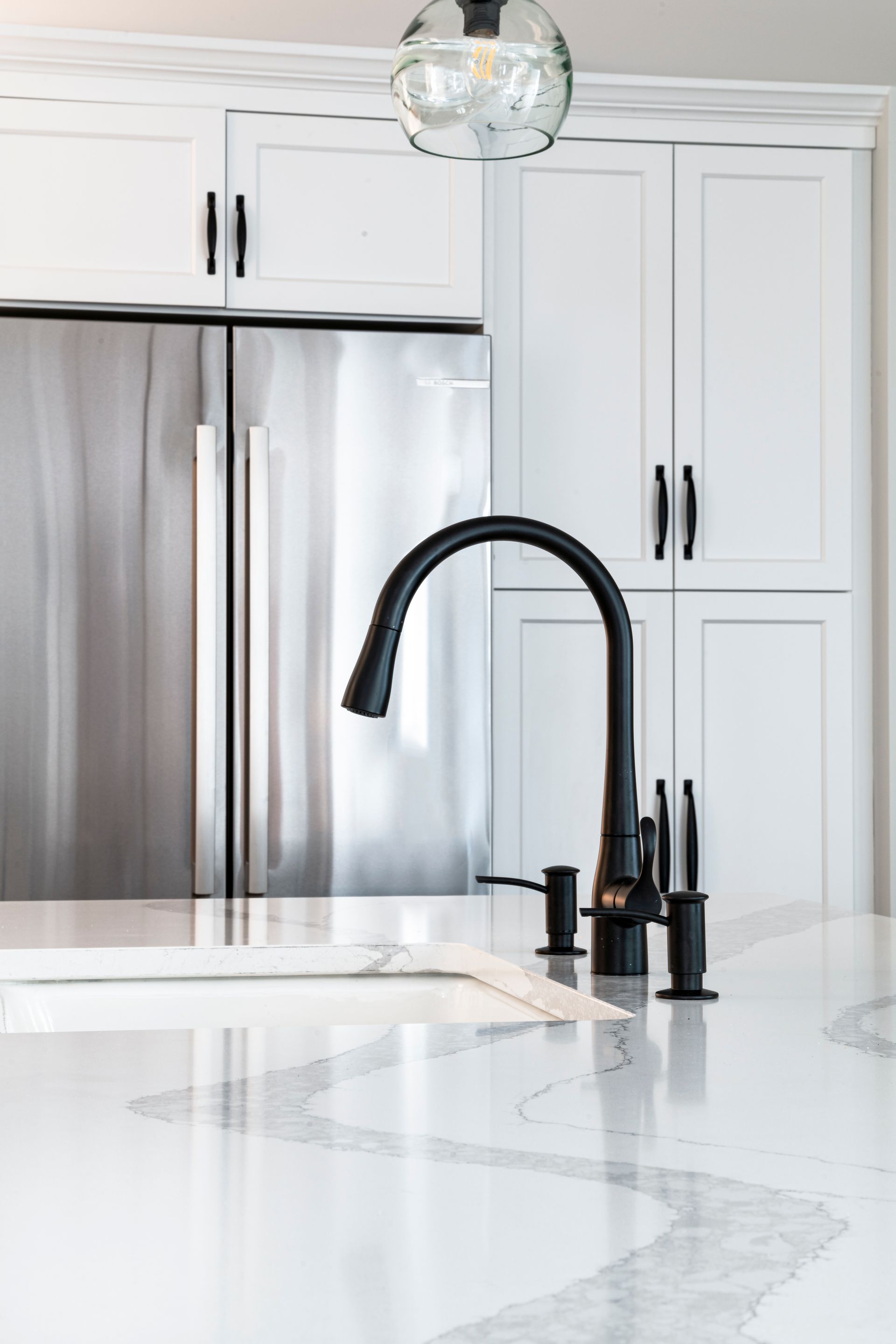 Modern kitchen with white cabinets, stainless fridge, marble island, and black gooseneck faucet