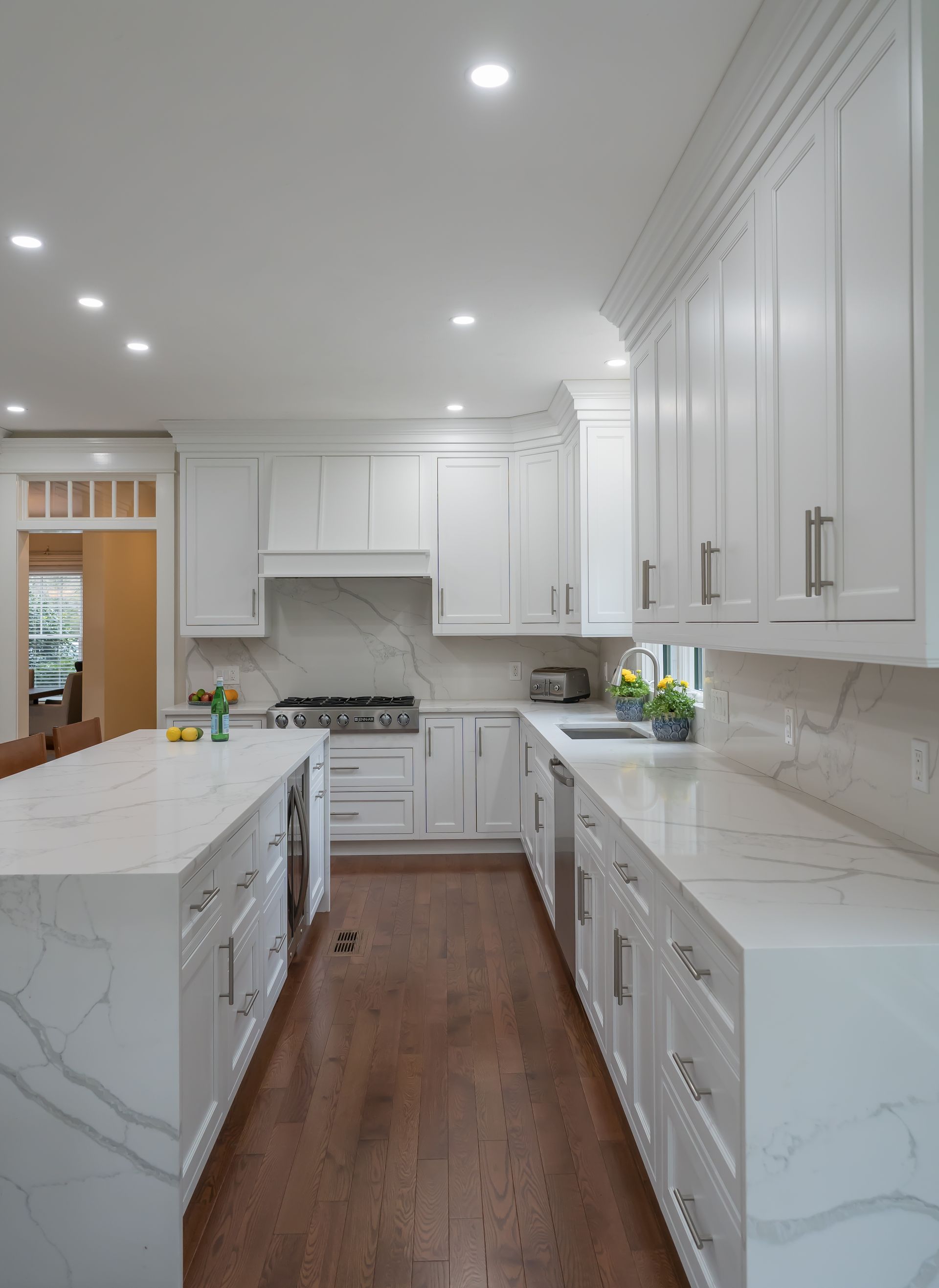 Bright white modern kitchen with marble countertops, wood floor, and stainless appliances