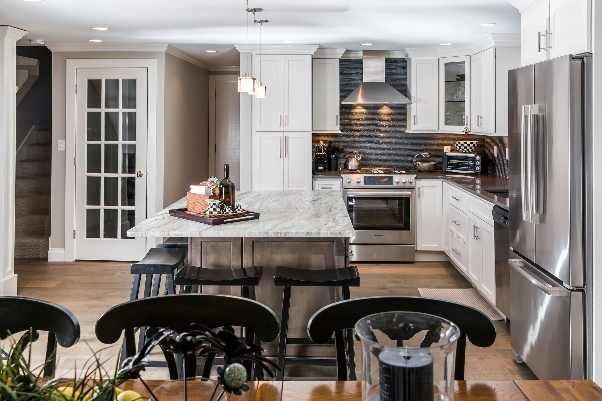 Modern white kitchen with stainless steel appliances, island, and bar stools; dining area in foreground