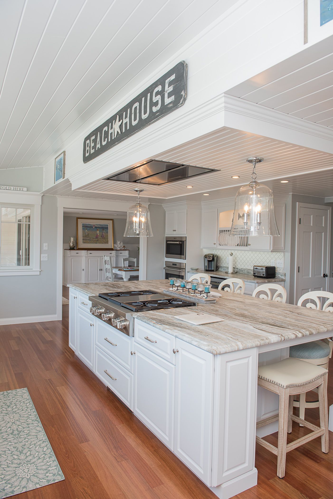 Bright white farmhouse kitchen with large island, wood floors, and a hanging “FARMHOUSE” sign