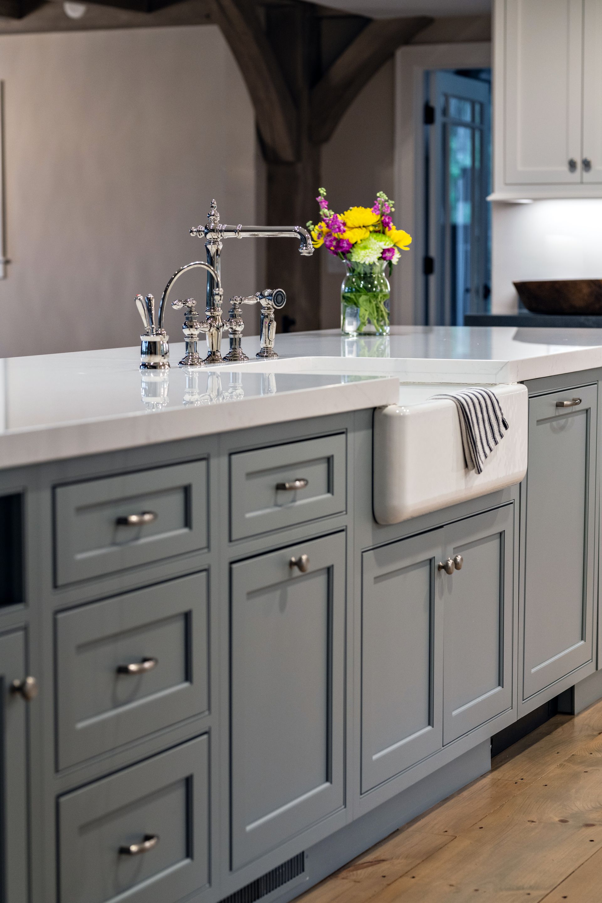 Gray kitchen island with white countertop, chrome faucet, and a vase of yellow flowers