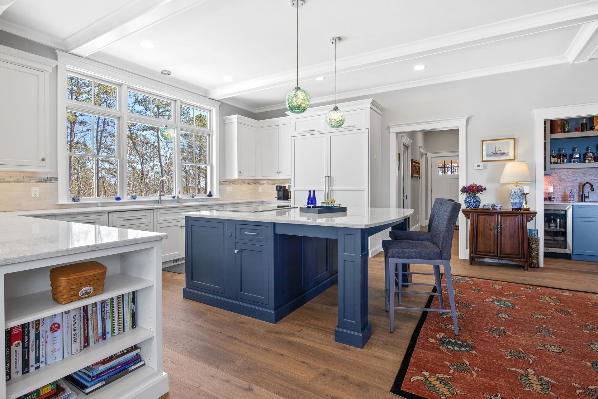 Bright kitchen with navy island, white cabinets, large windows, and red patterned rug