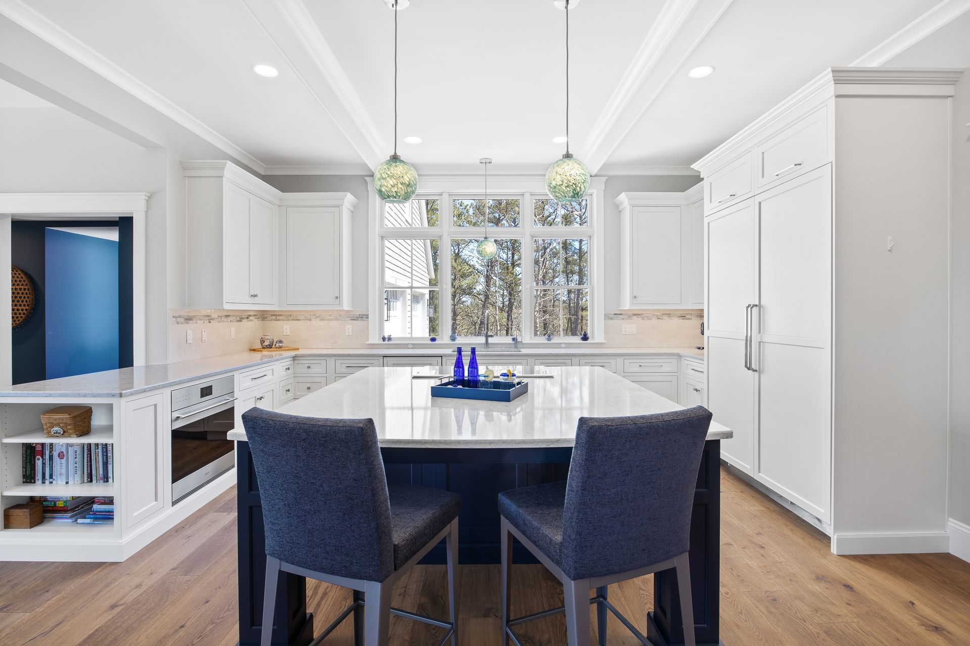 Bright white kitchen with an island, navy chairs, pendant lights, and hardwood floors