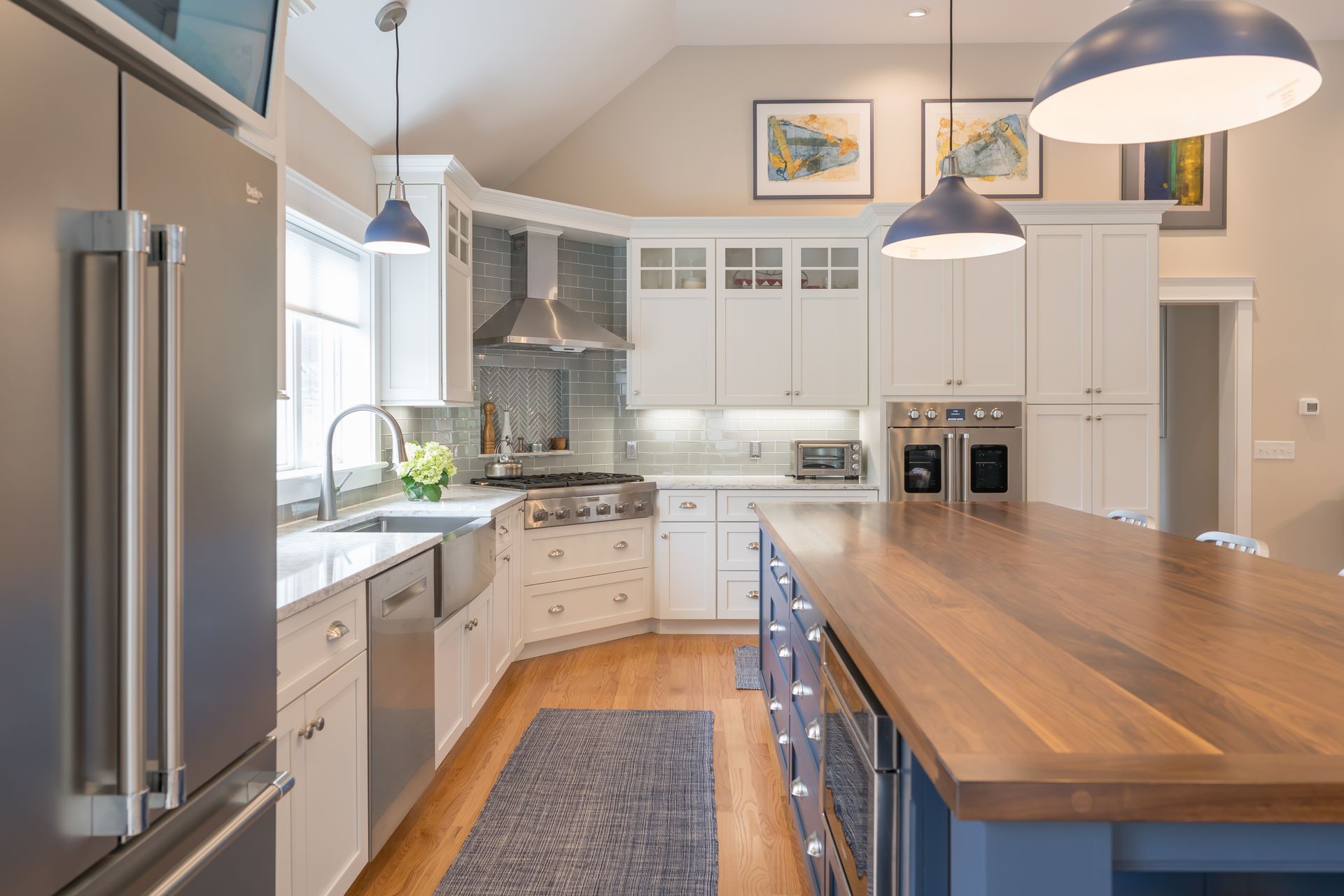 Bright modern kitchen with white cabinets, stainless fridge, and a large wooden island.