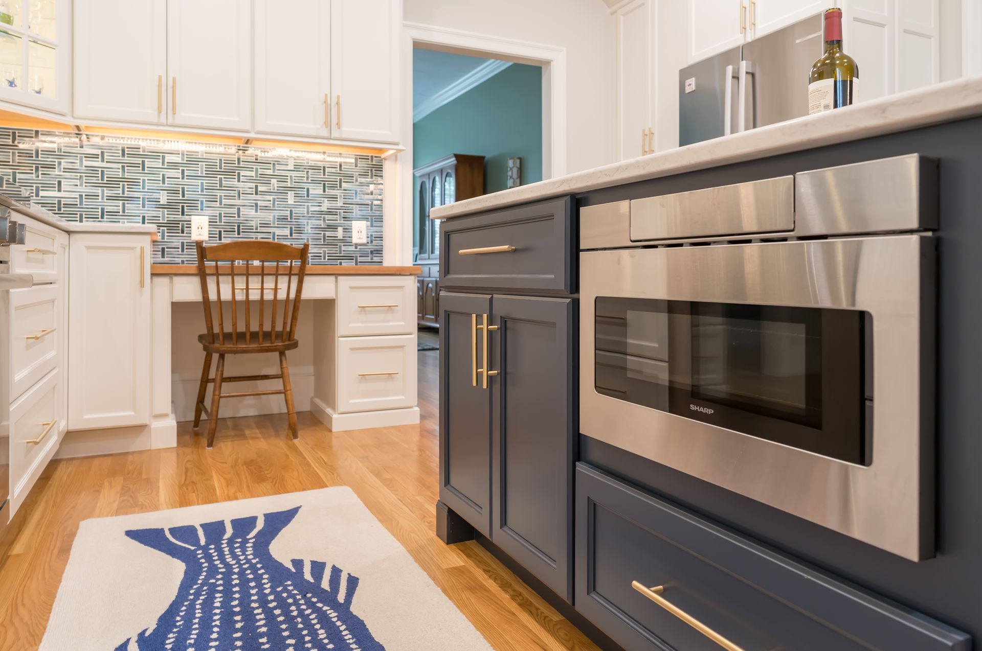 Bright kitchen with stainless steel appliances, white cabinets, blue rug, and a small wooden chair at the island.