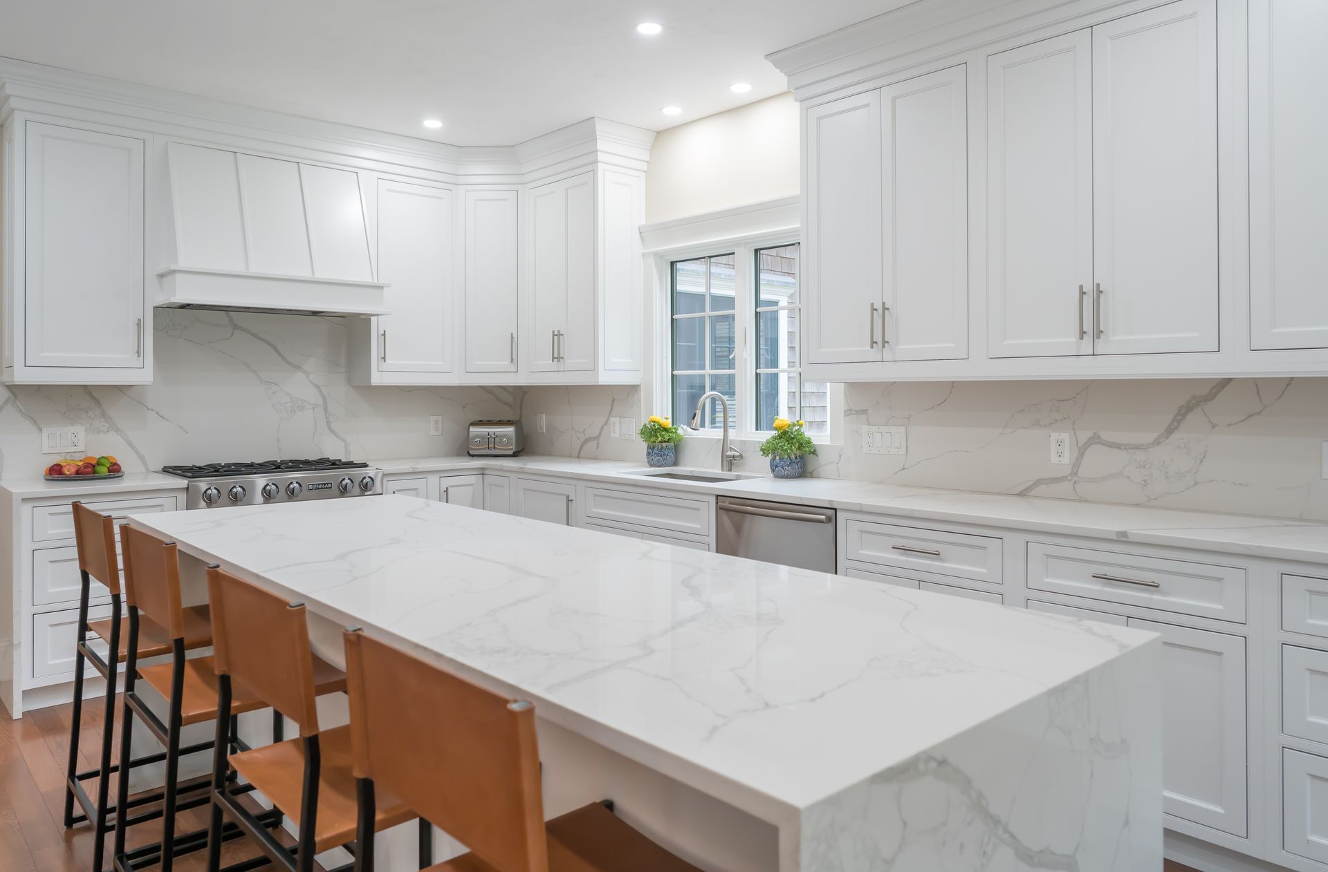 Bright white modern kitchen with marble island, white cabinets, and a window over the sink.