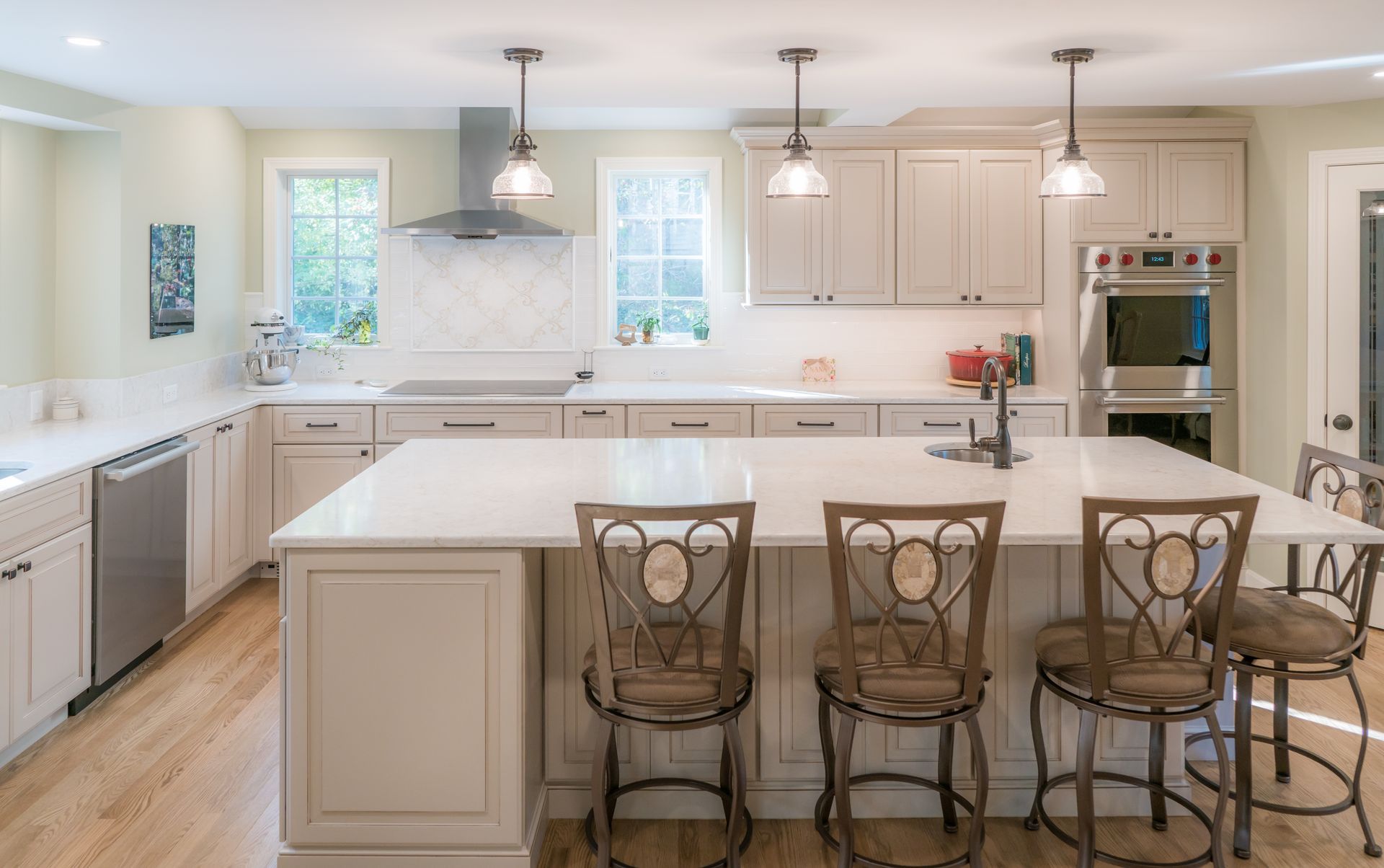 Bright modern kitchen with white cabinets, large island, and four bar stools under pendant lights
