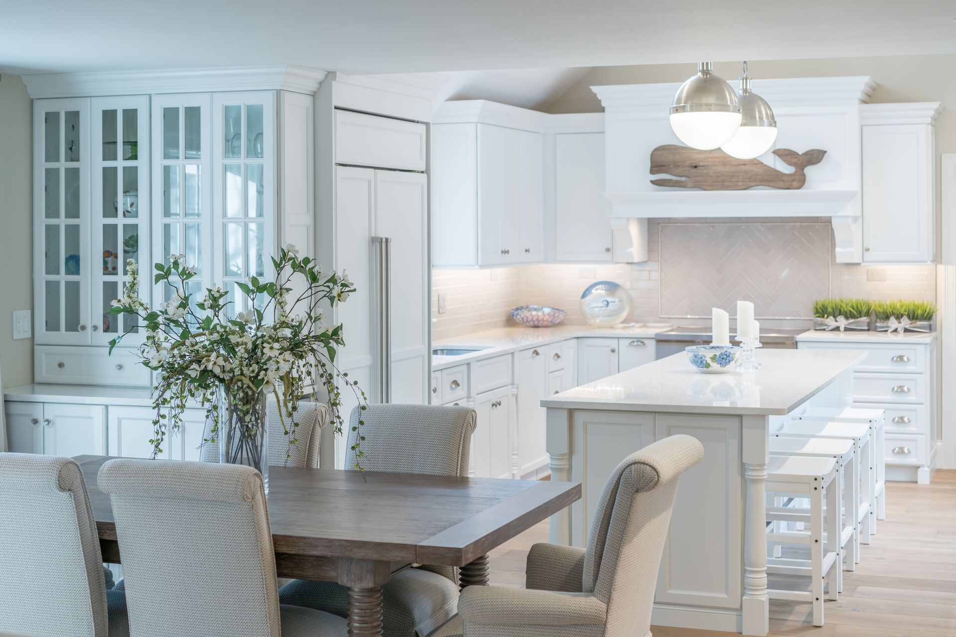 Bright white kitchen with island, glass-front cabinets, dining table, and hanging light over a rustic decor scene