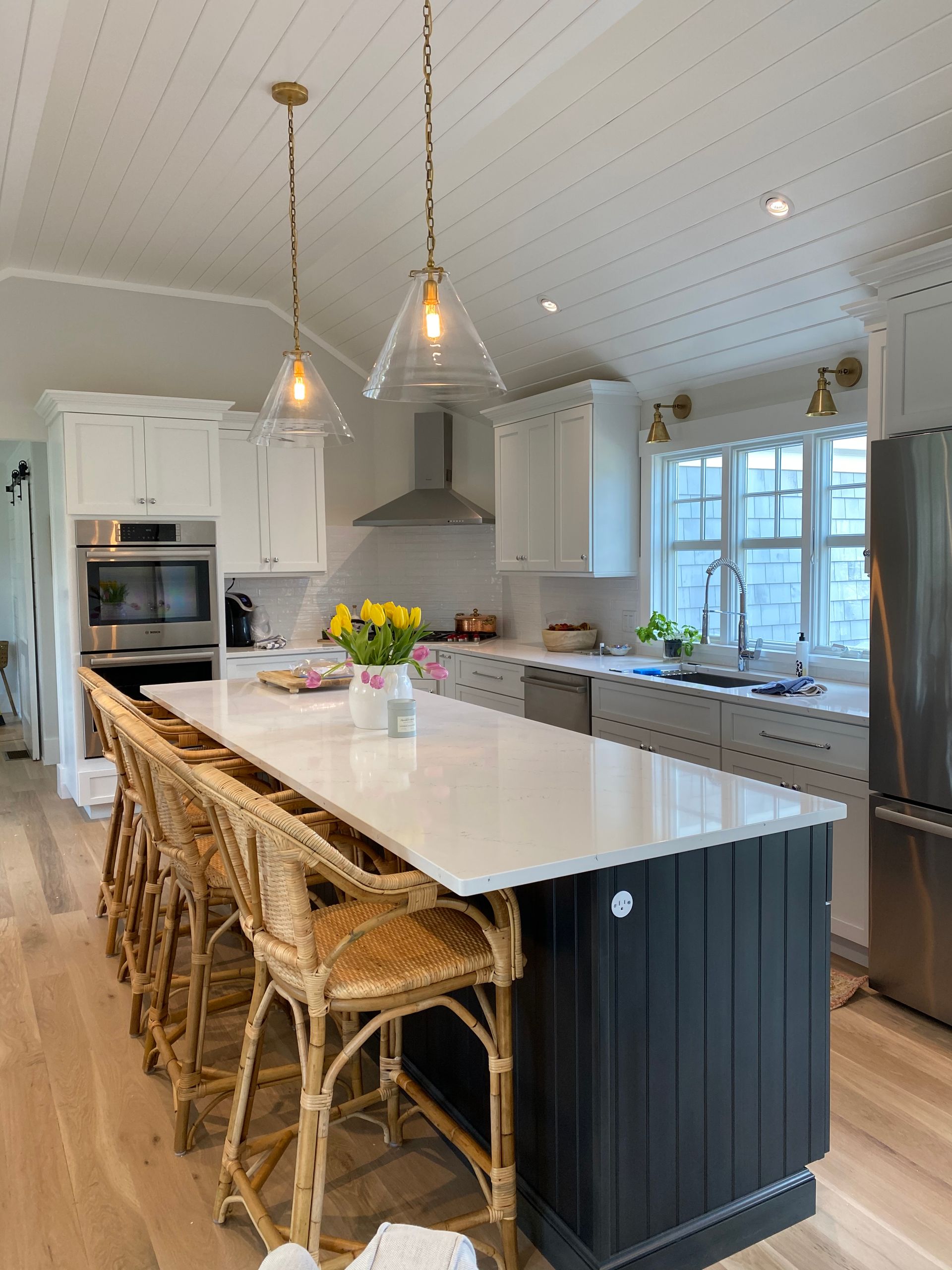 Bright white kitchen with marble island, woven stools, pendant lights, and large windows