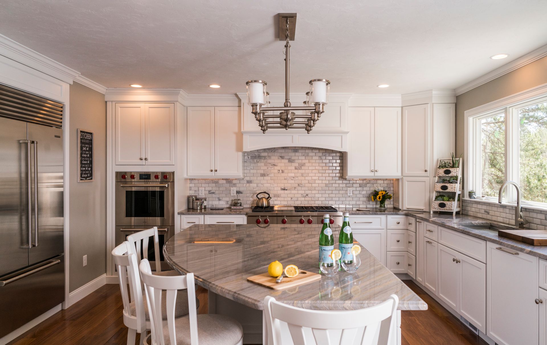 Bright kitchen with white cabinets, marble island, chandelier, and a large window.