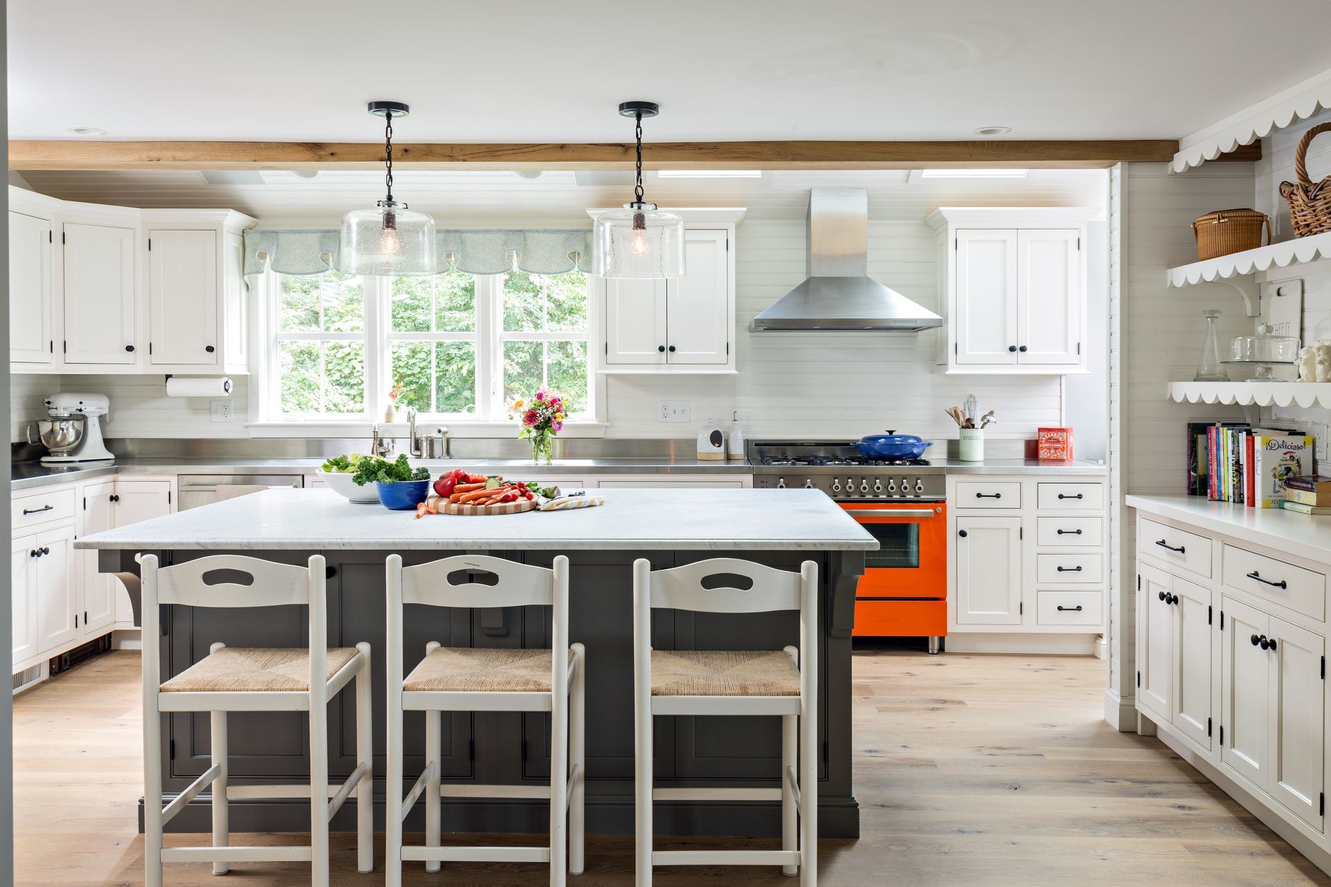 Bright modern kitchen with white cabinets, an island, orange stove, and pendant lights