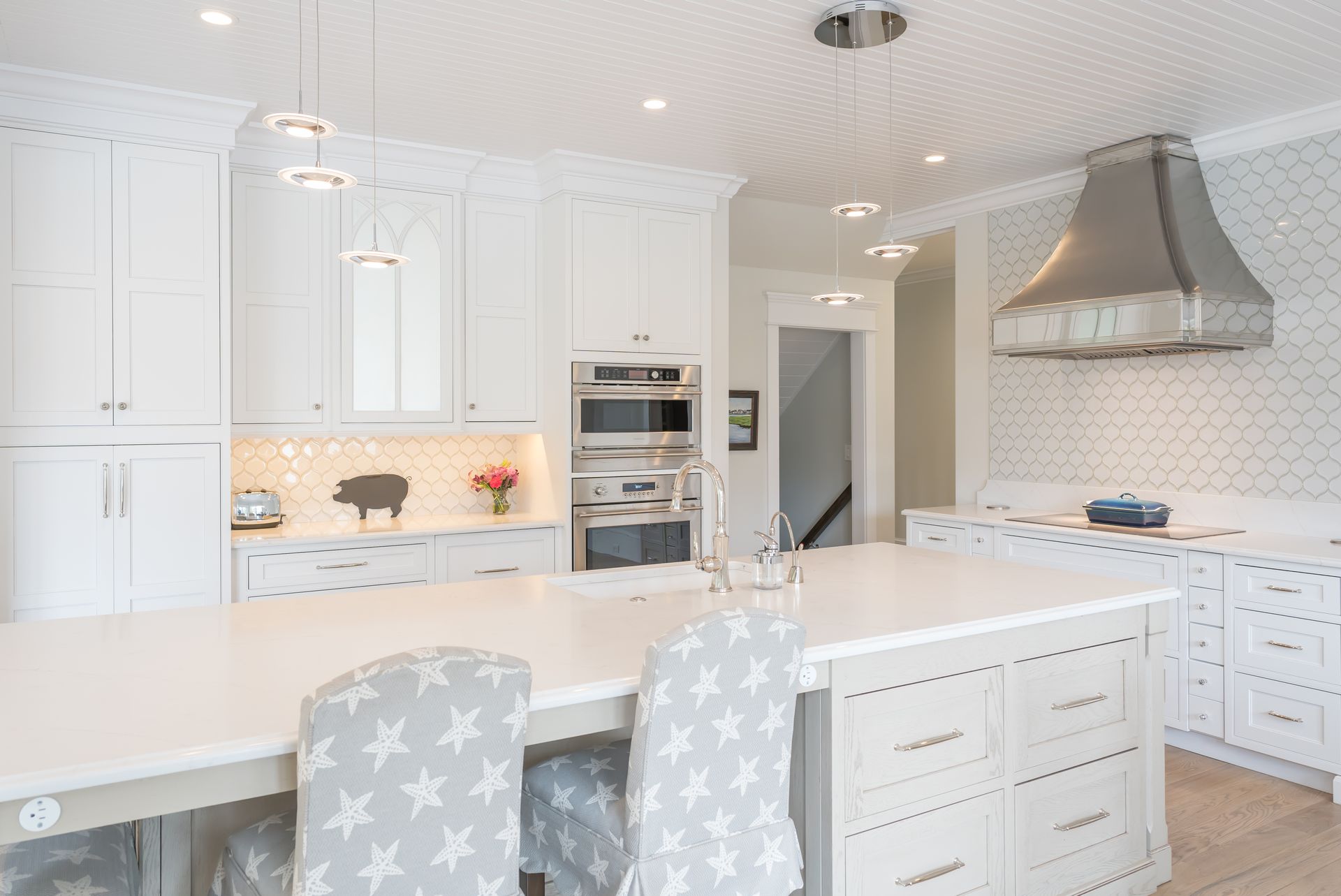 Bright white modern kitchen with large island, pendant lights, built-in appliances, and marble countertops
