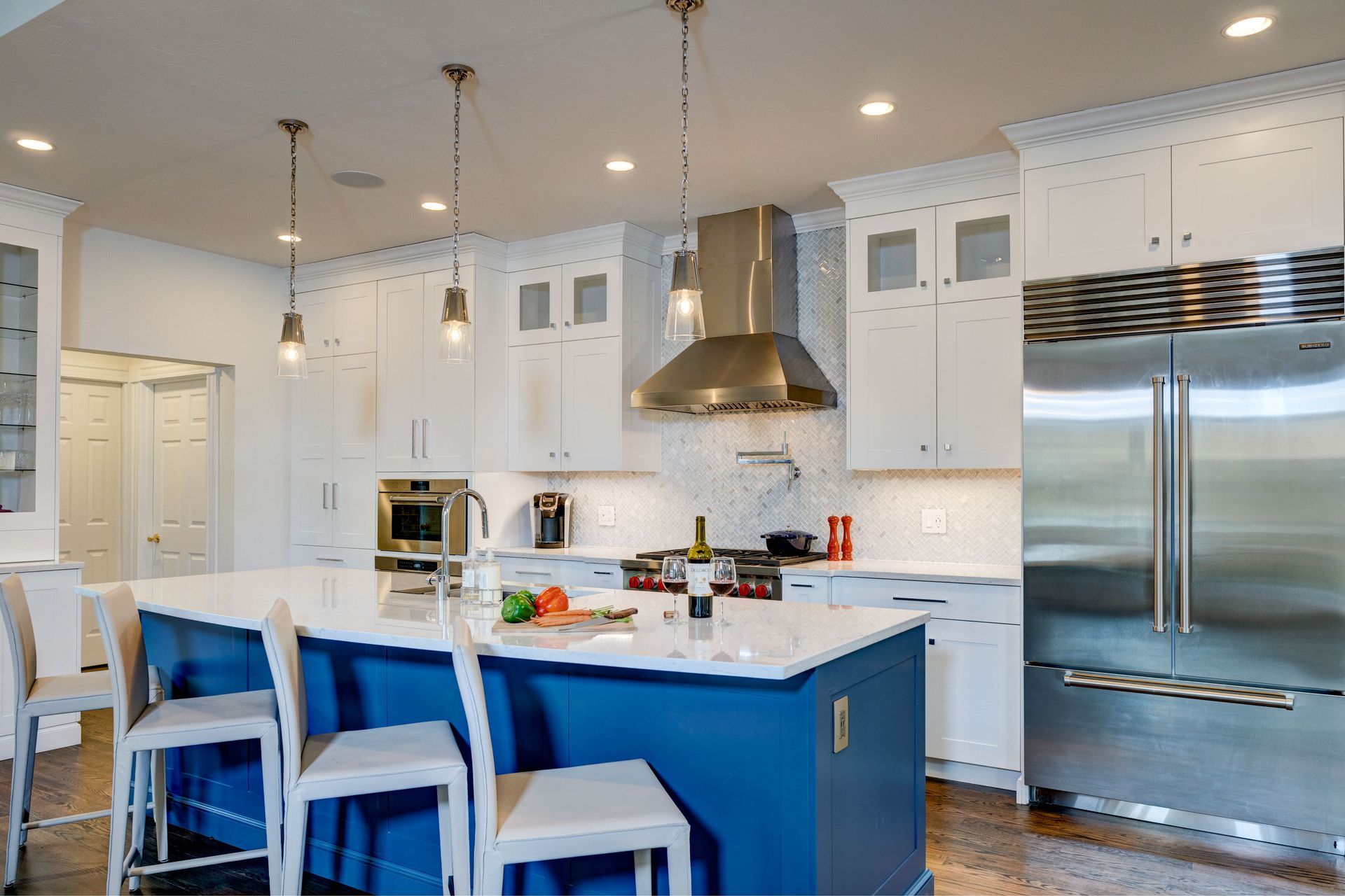 Bright white kitchen with blue island, stainless steel appliances, and two white barstools