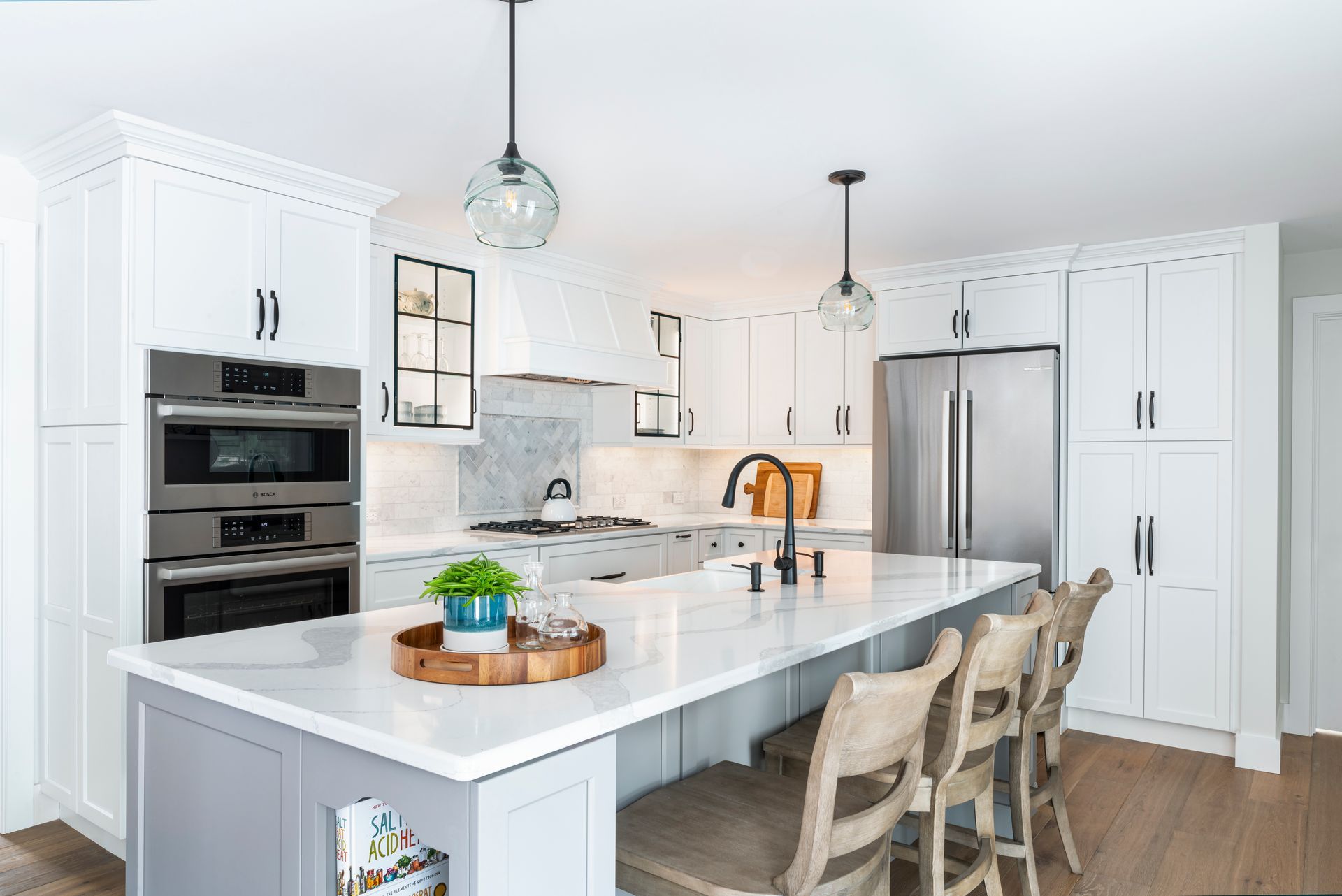 Bright white modern kitchen with island, stainless appliances, pendant lights, and wooden barstools
