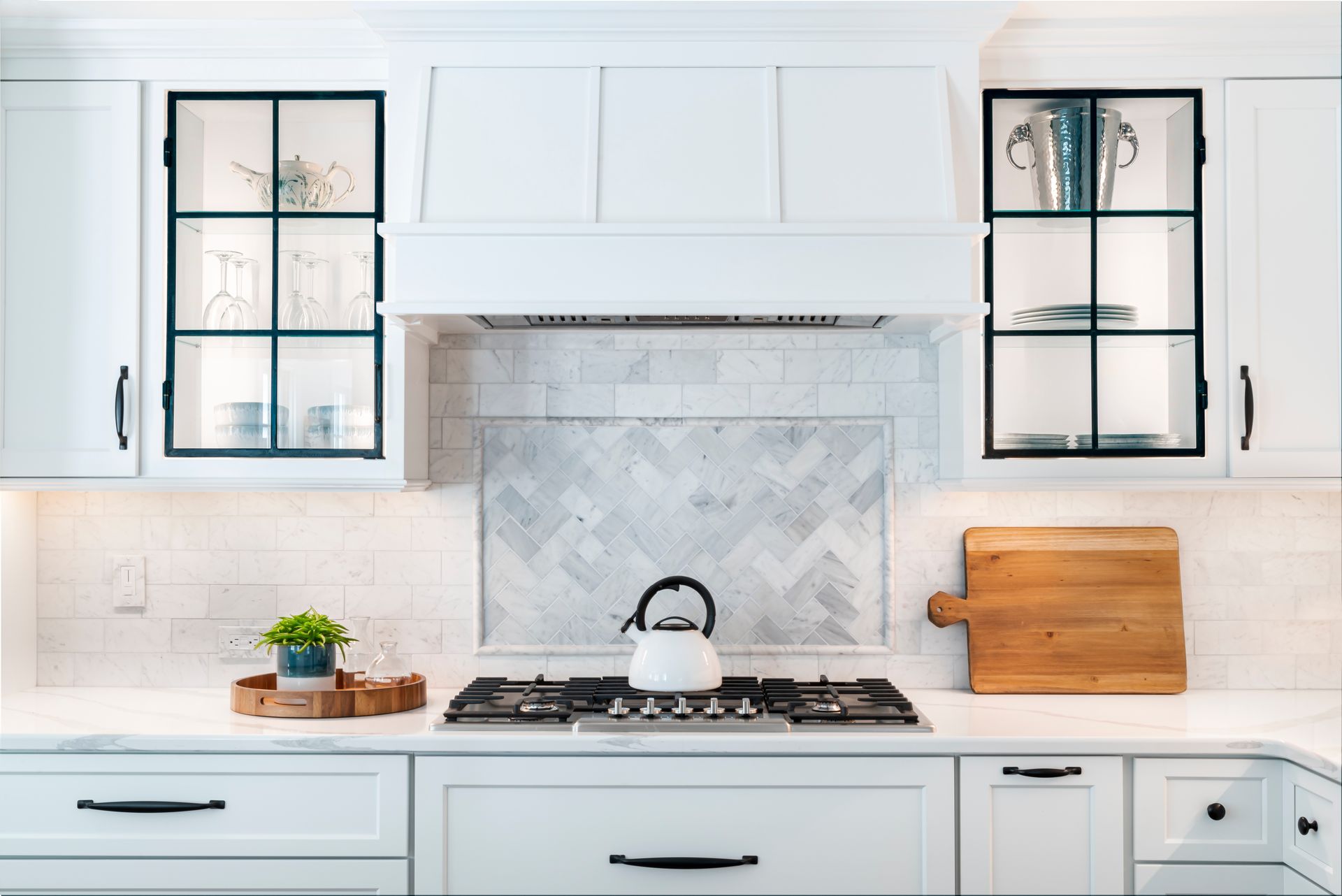 Modern white kitchen with black-trimmed cabinets, gas stove, kettle, and wood cutting boards
