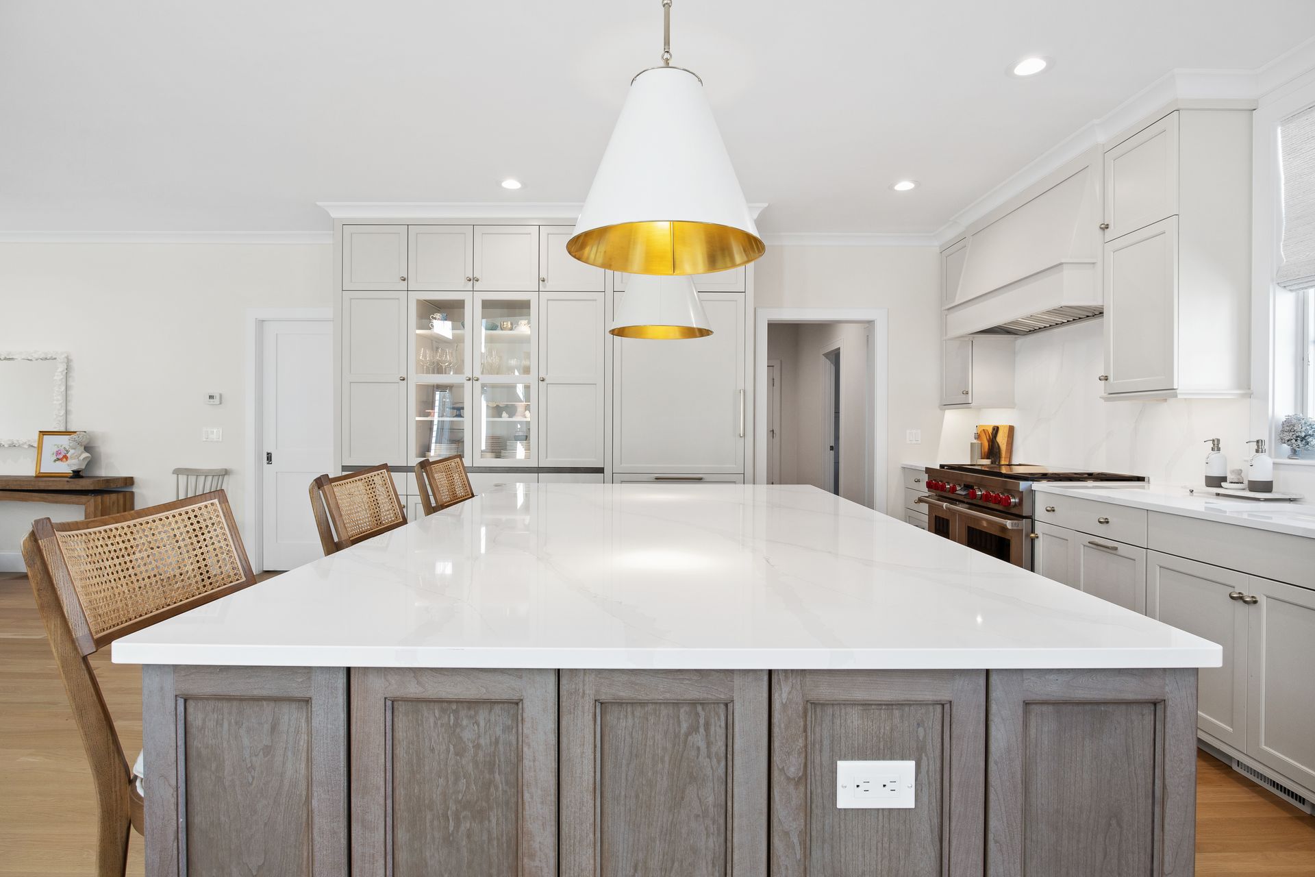 Bright modern kitchen with white island, gray cabinets, wicker stools, and brass pendant lights