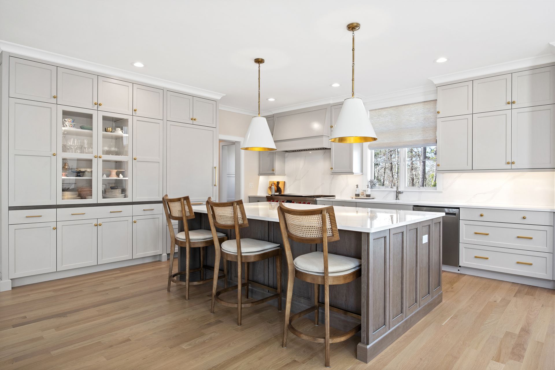Bright modern kitchen with gray cabinets, island seating, pendant lights, and hardwood floors