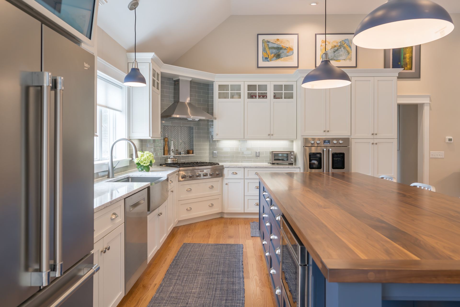Bright modern kitchen with stainless steel fridge, white cabinets, and a large wooden island under pendant lights