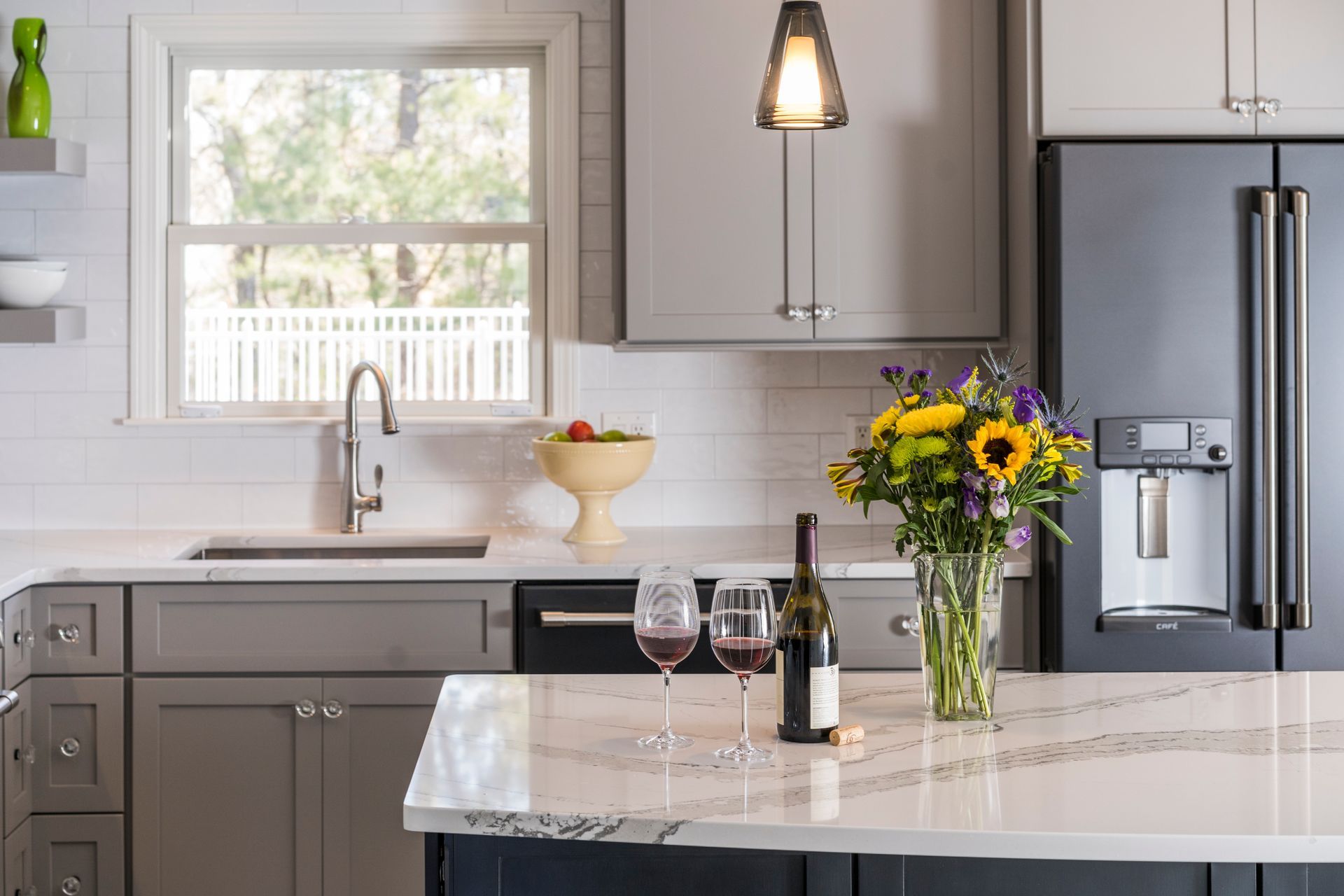 Modern kitchen with gray cabinets, white island, stainless fridge, and a vase of sunflowers on the counter