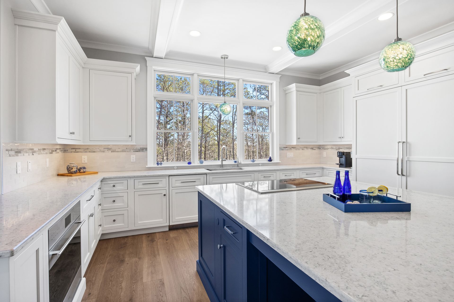 Bright white kitchen with blue island, large window, and green pendant lights