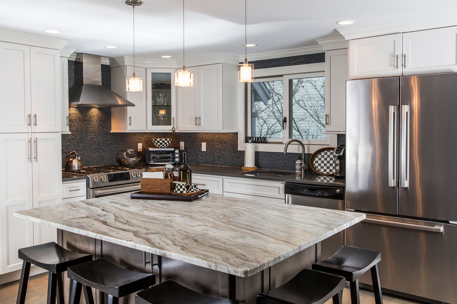 Modern white kitchen with marble island, stainless steel appliances, pendant lights, and black stools