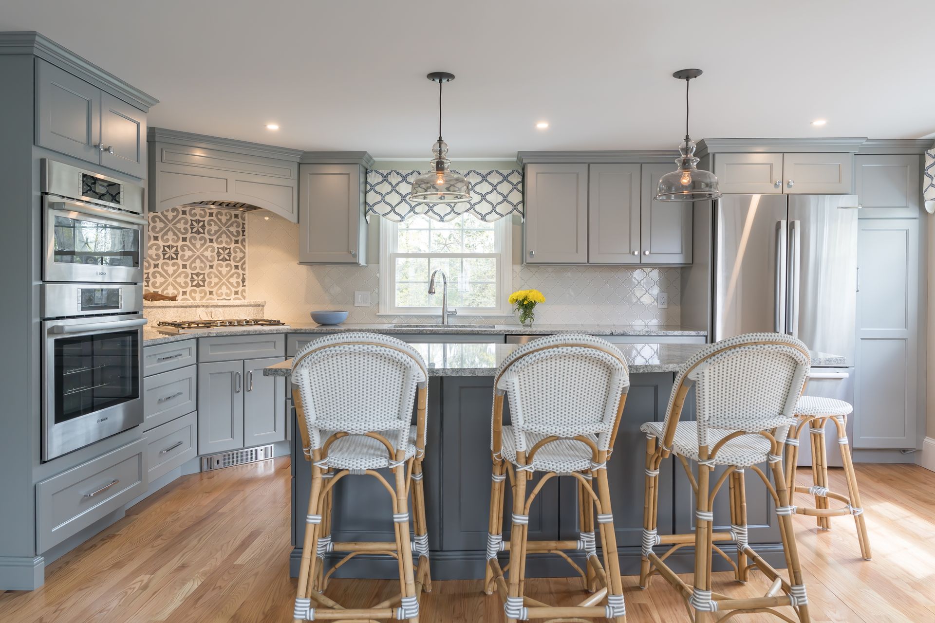 Bright gray kitchen with island, wicker bar stools, pendant lights, and stainless steel appliances