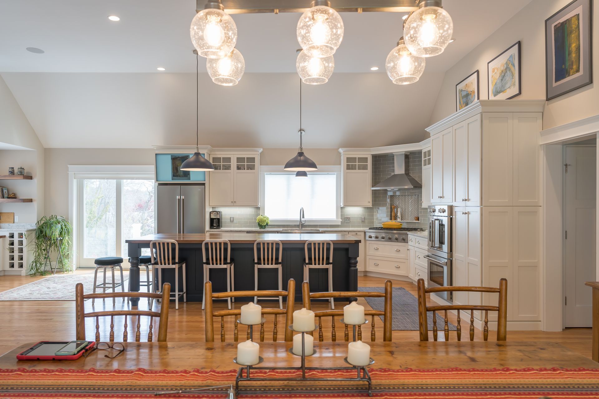 Bright open-concept kitchen and dining room with bar stools, white cabinets, and hanging globe lights.