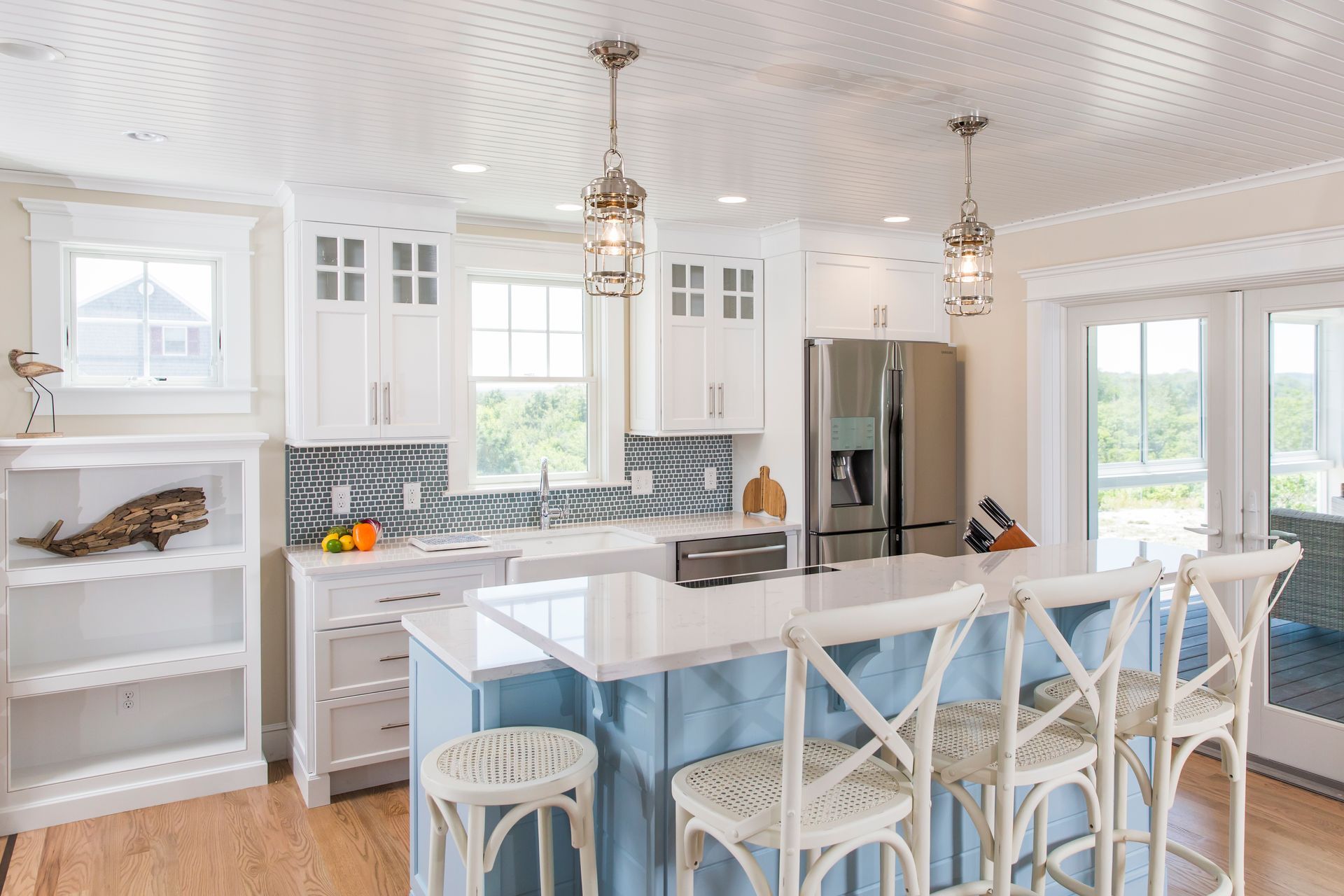 Bright white kitchen with island, bar stools, pendant lights, and large windows