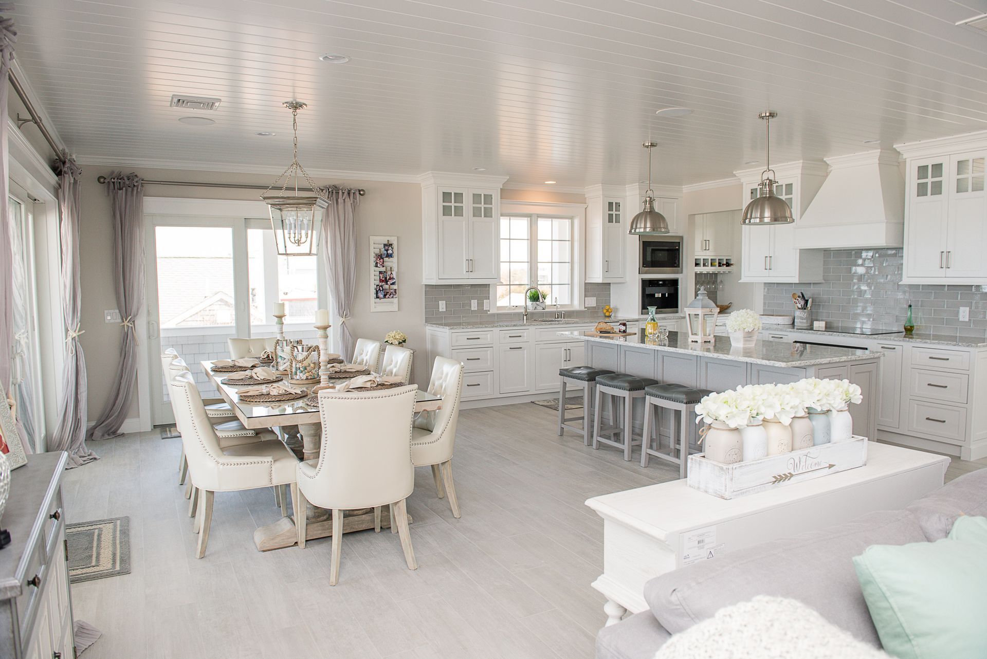 Bright white open-plan kitchen and dining room with large windows and a table set for a meal.