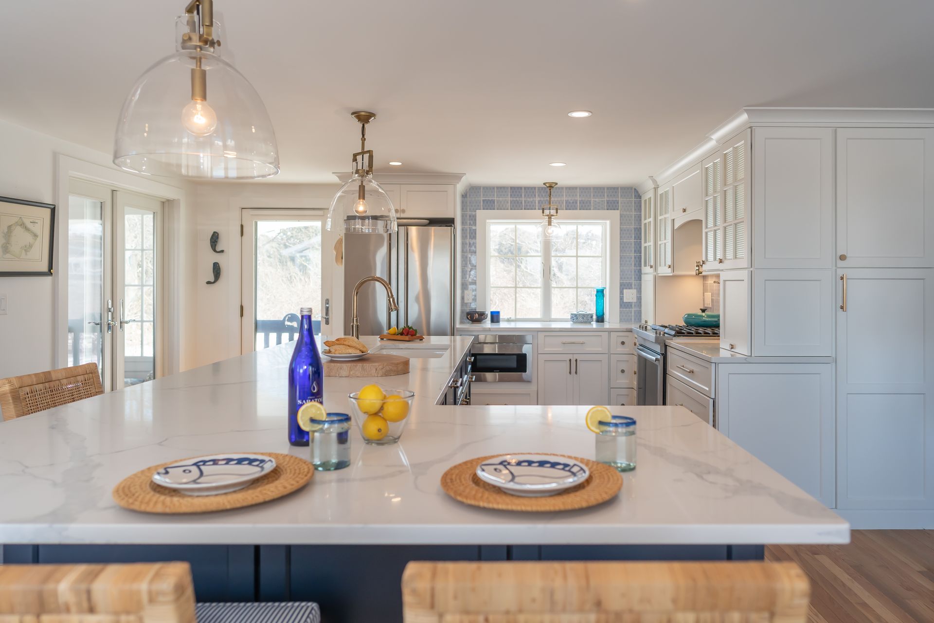 Bright modern kitchen with white island, blue vase, pendant lights, and set dining plates