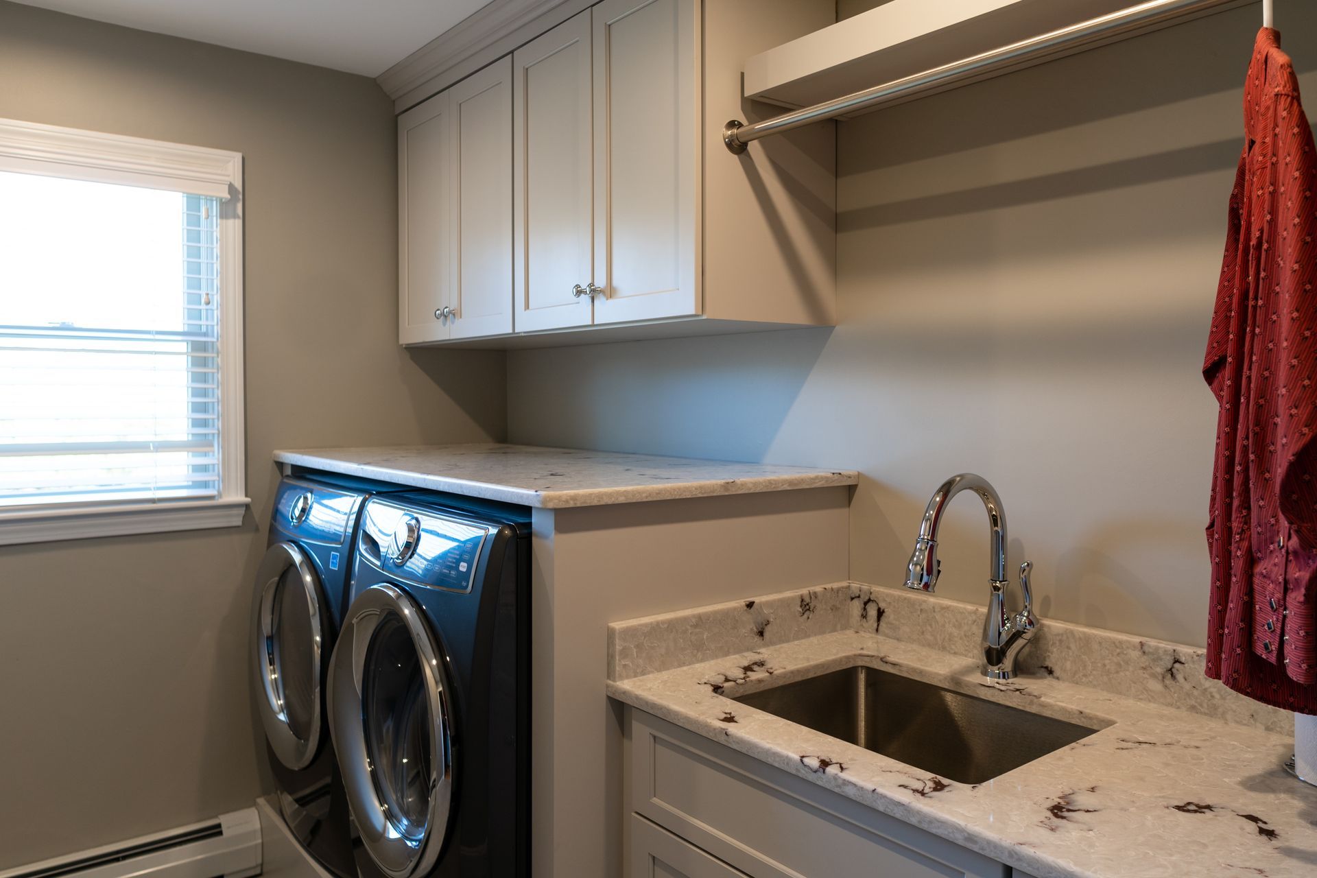 Laundry room with front-load washer and dryer, utility sink, cabinets, and a red towel hanging nearby