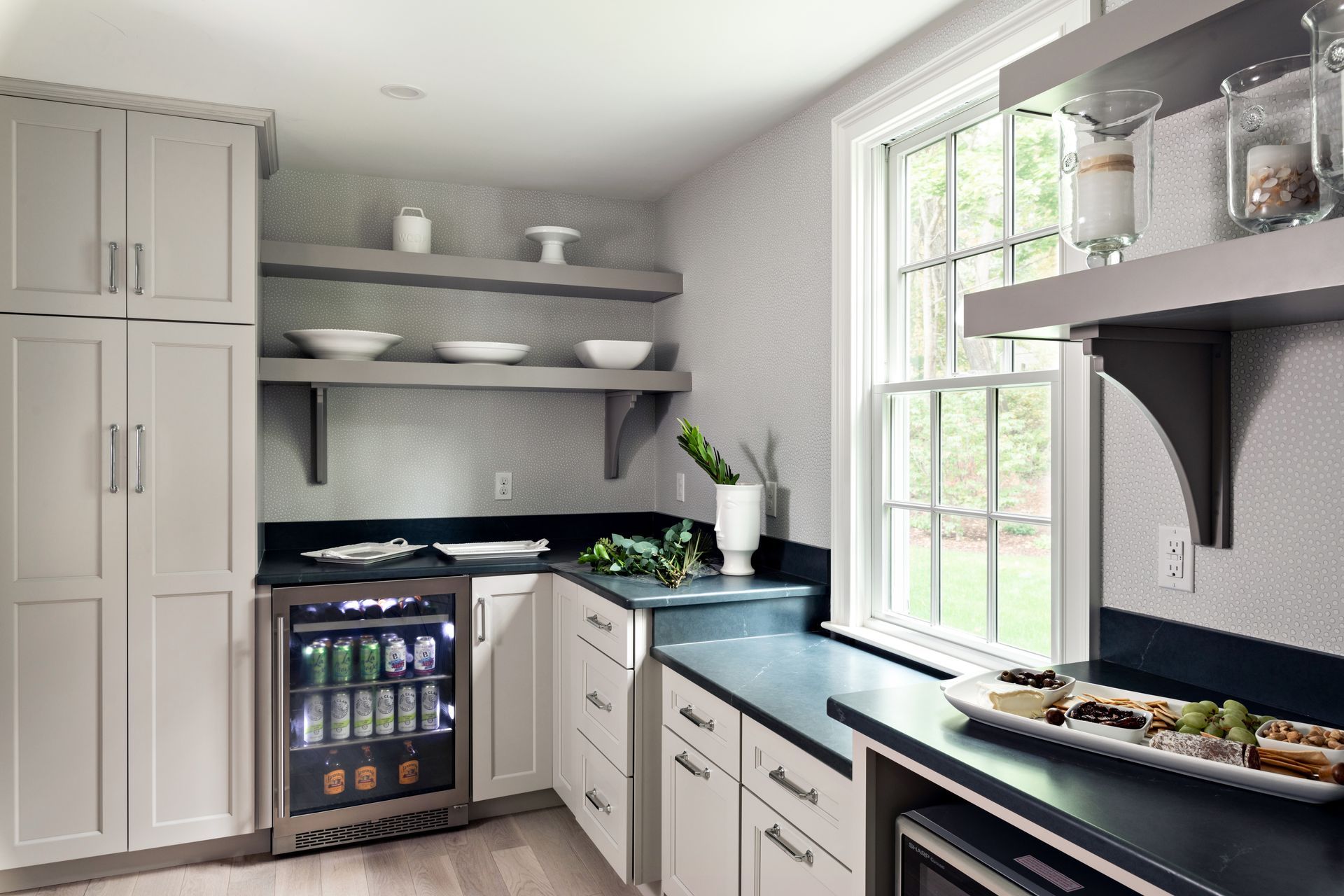 Bright modern kitchen with gray cabinets, open shelves, black countertops, and a window over the sink.
