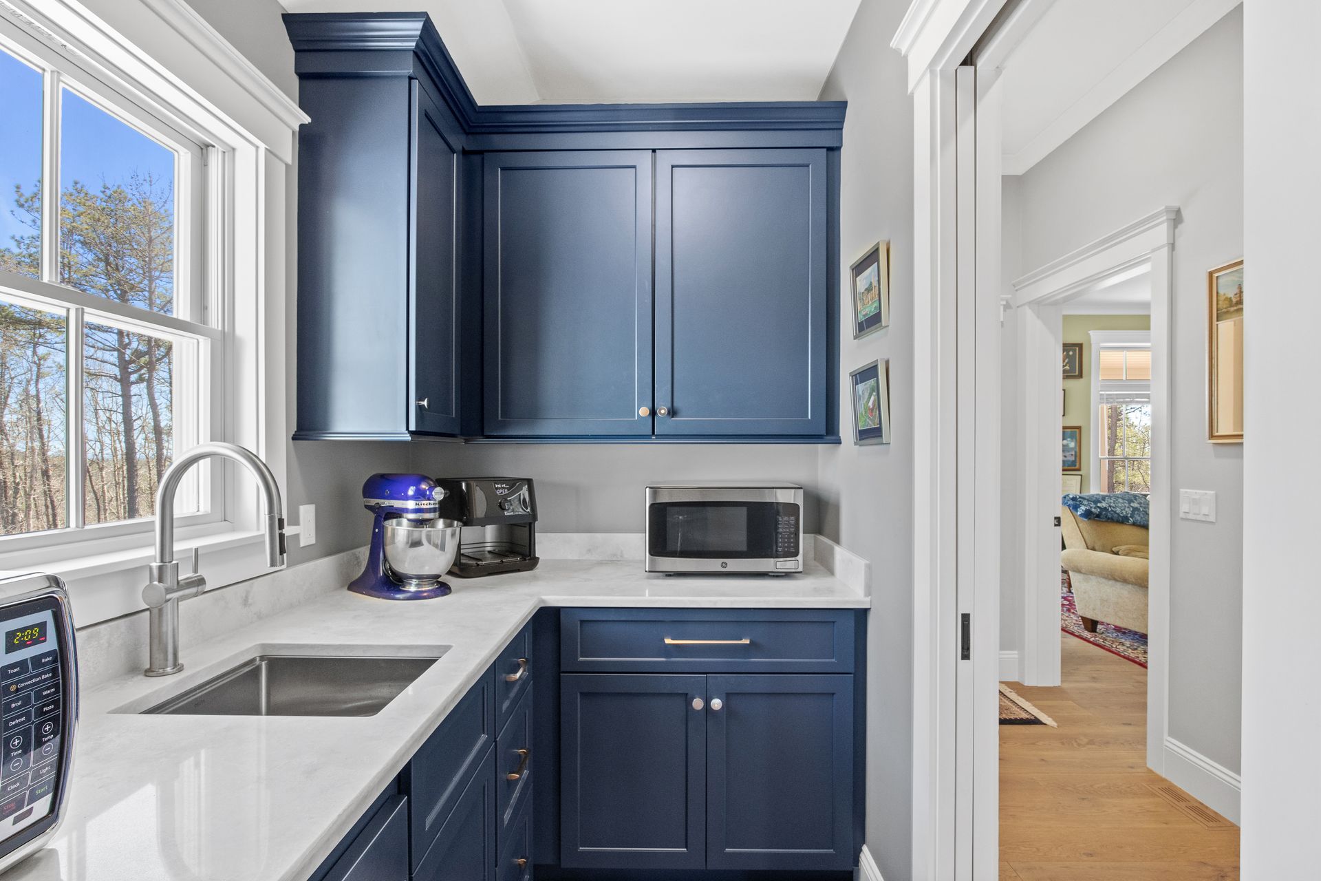 Bright kitchen with navy cabinets, white counters, window light, and a doorway to a nearby room
