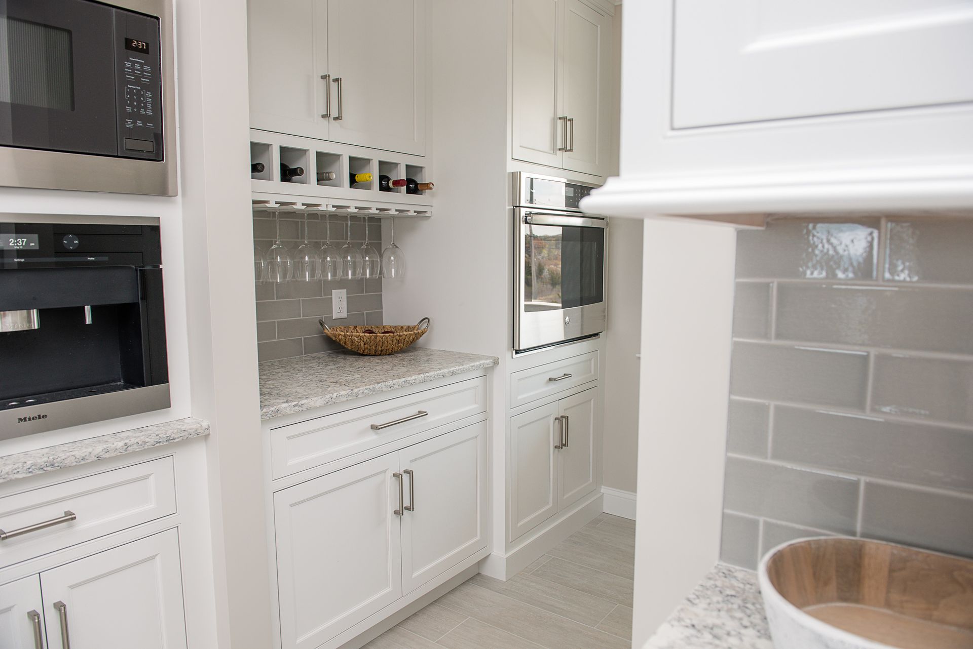 Bright white kitchen with built-in ovens, tile backsplash, and a counter nook with jars and a wooden bowl