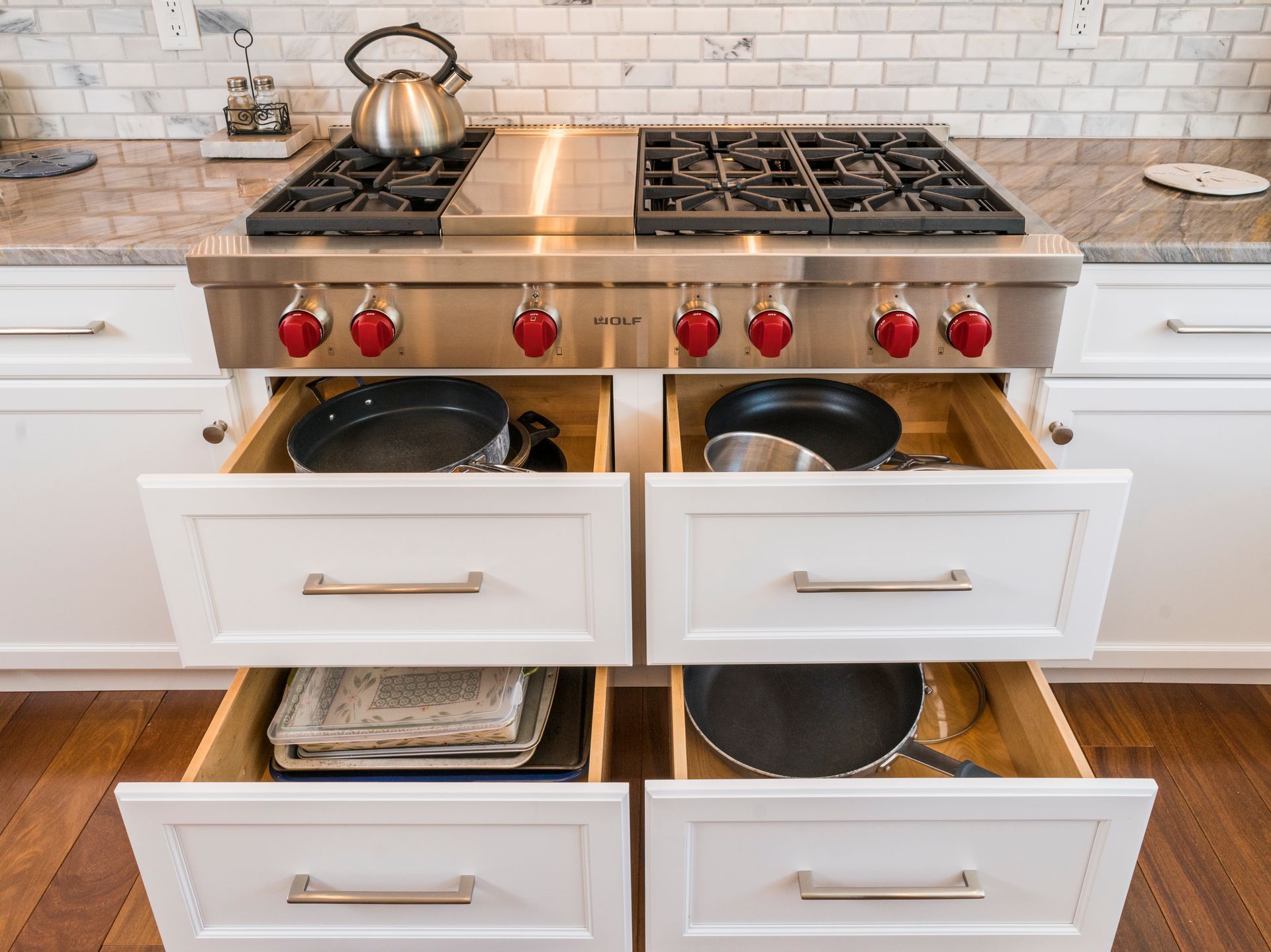 Kitchen range with two ovens, red knobs, and white cabinets in a tiled backsplash setting