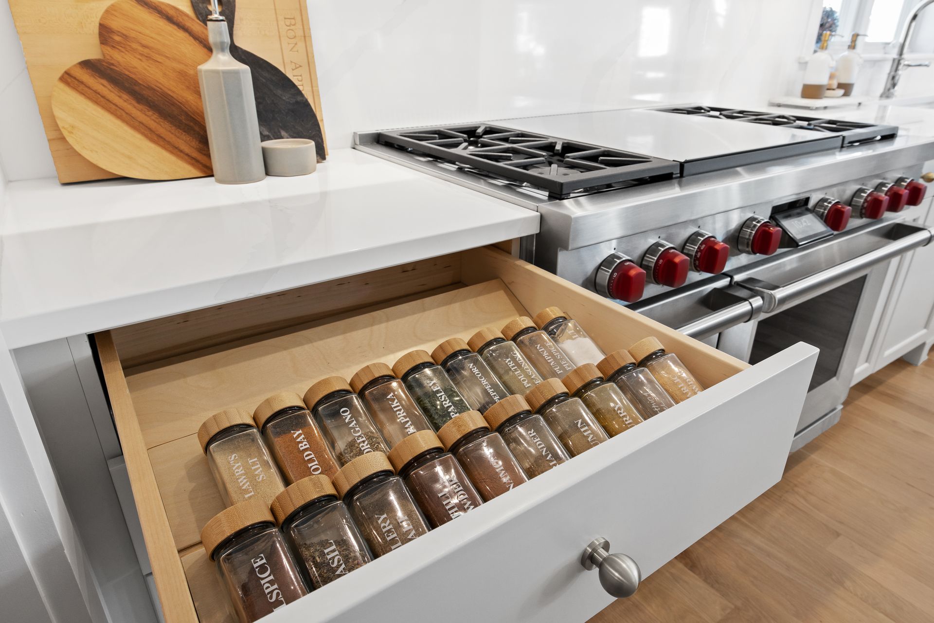Kitchen drawer with organized spice jars beside a stainless steel stove and white countertop