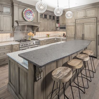 Elegant gray kitchen with large island, stone countertops, and five round stools under pendant lights