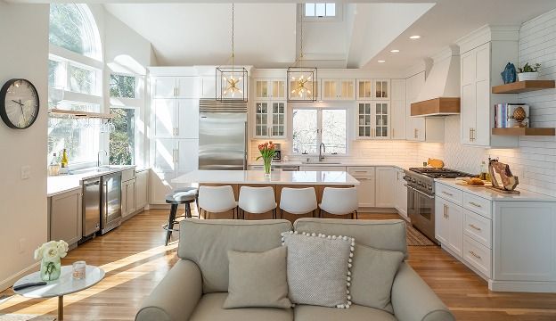 Bright modern kitchen and dining area with white cabinets, wooden floors, and a sofa in the foreground