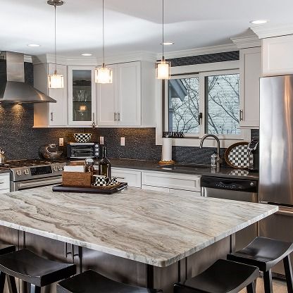 Bright modern kitchen with white cabinets, stainless appliances, and a large marble island with stools.
